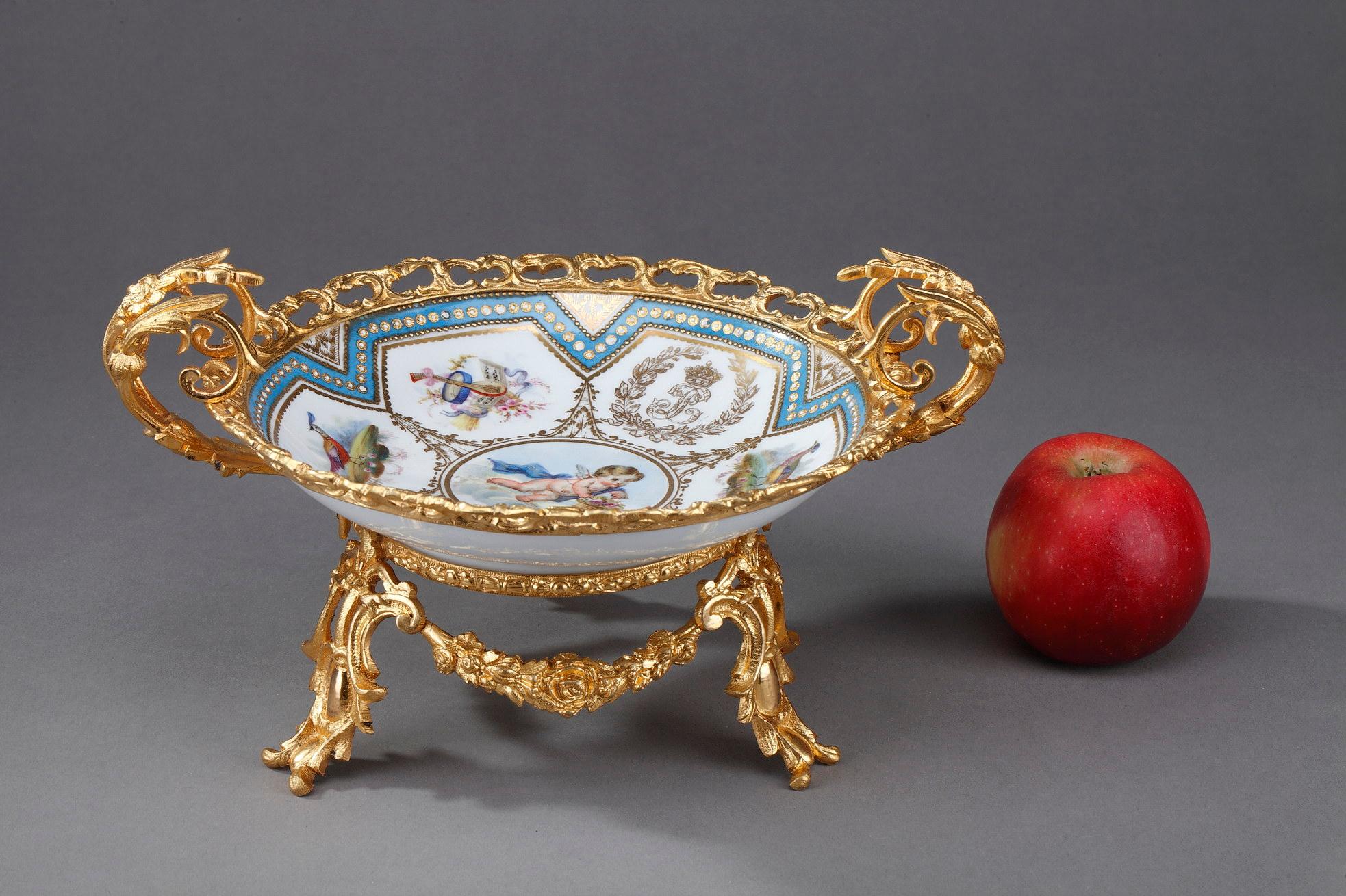 Sevres porcelain bowl with a gilded bronze mount. It is decorated with a winged and draped cupid seated on a cloud surrounded by bouquets of flowers, an allegory of the gardener, an allegory of music and the mark of King Louis-Philippe surmounted by
