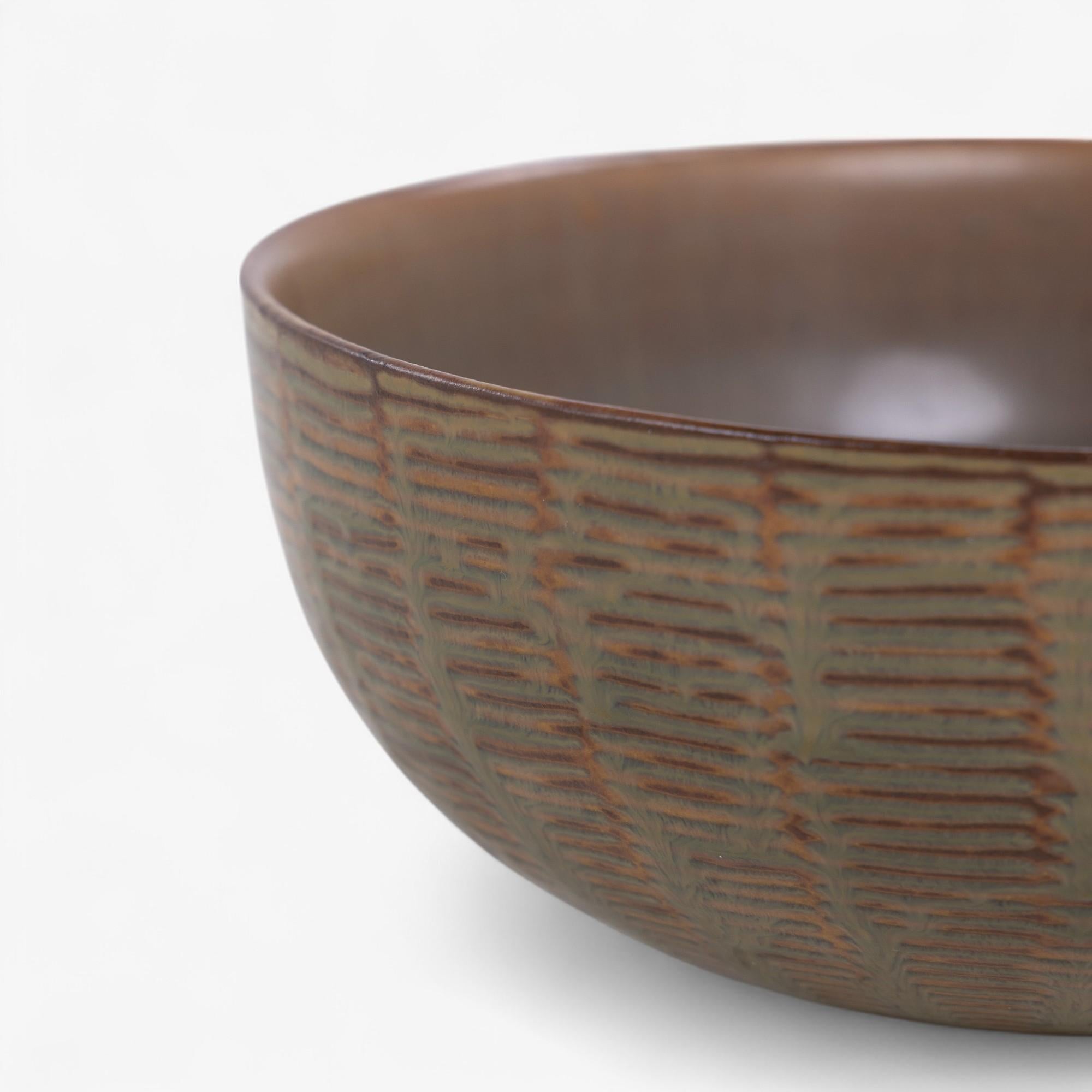 Circular stoneware bowl with an outer surface with horizontal patterns in relief. Decorated with a green-brown glaze (model 20717). Designed in 1944. Signed.