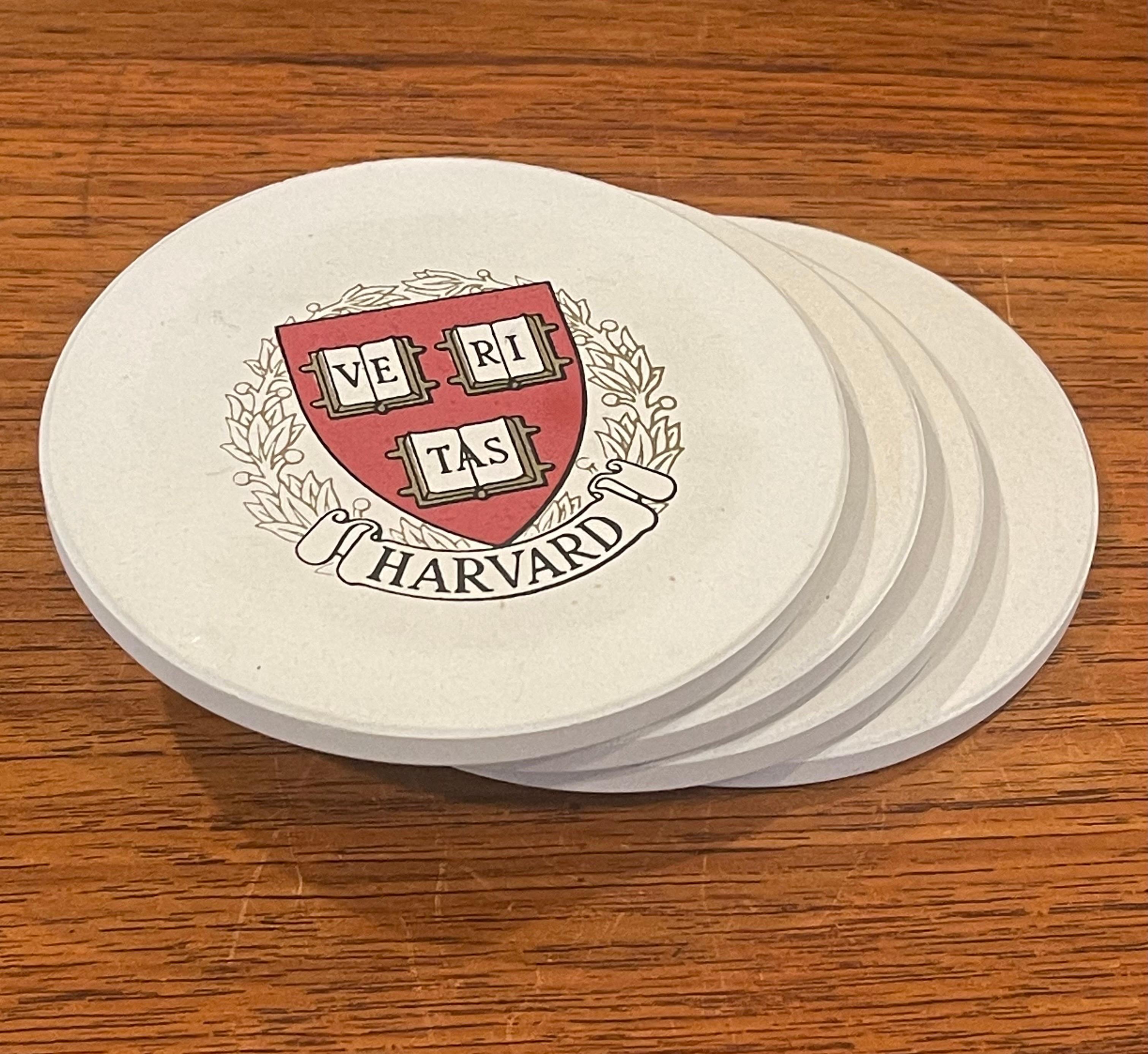Vintage box set of four Harvard University stone drink coasters by Coaster Stone, circa 1980s. The set comes with the original box and includes four round cream colored stone coasters with the Harvard University seal; the coasters are 4.25