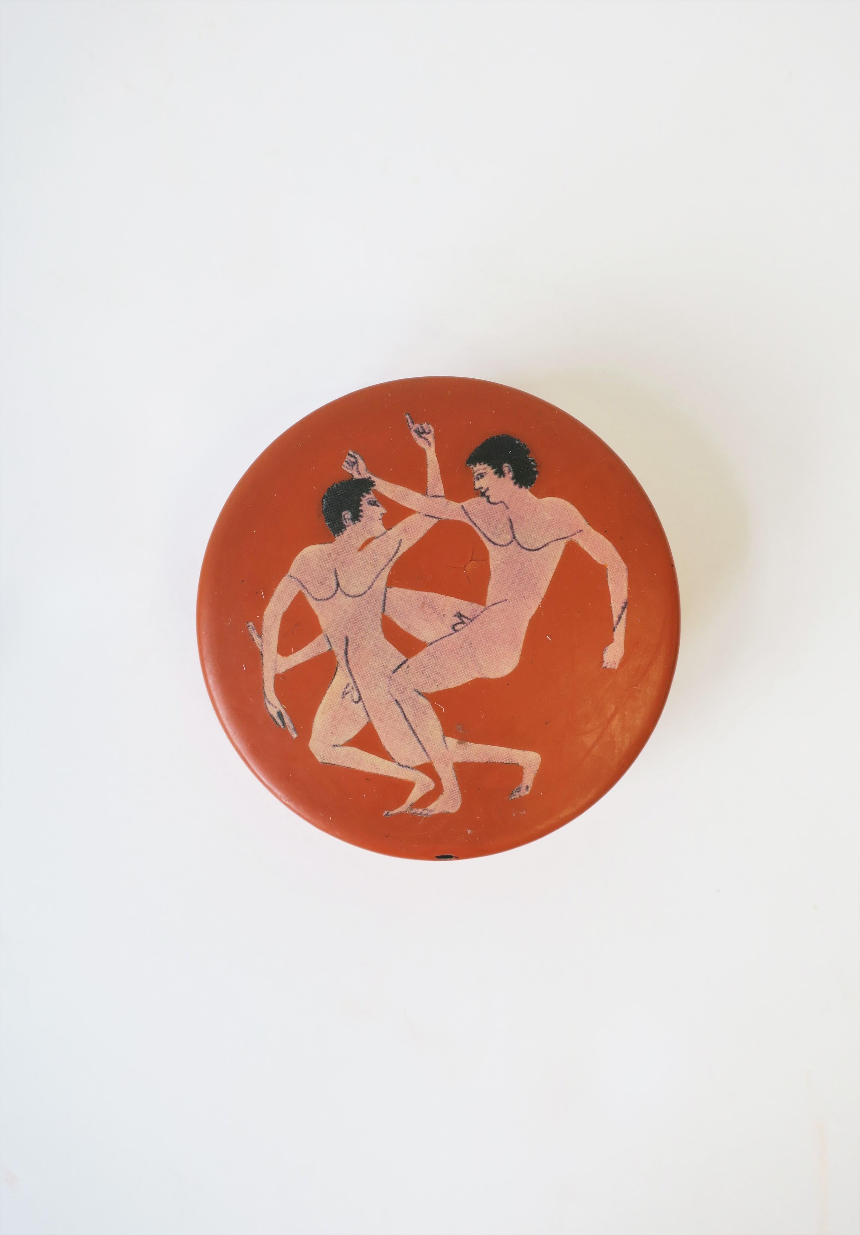 A round box, decorative or jewelry, with Greco-Roman nude male figurative design, circa 20th century. Boxes exterior has an orange/terracotta hue with two nude male figures on top/lid. Interior is a high-gloss black lacquer. Box is great to hold