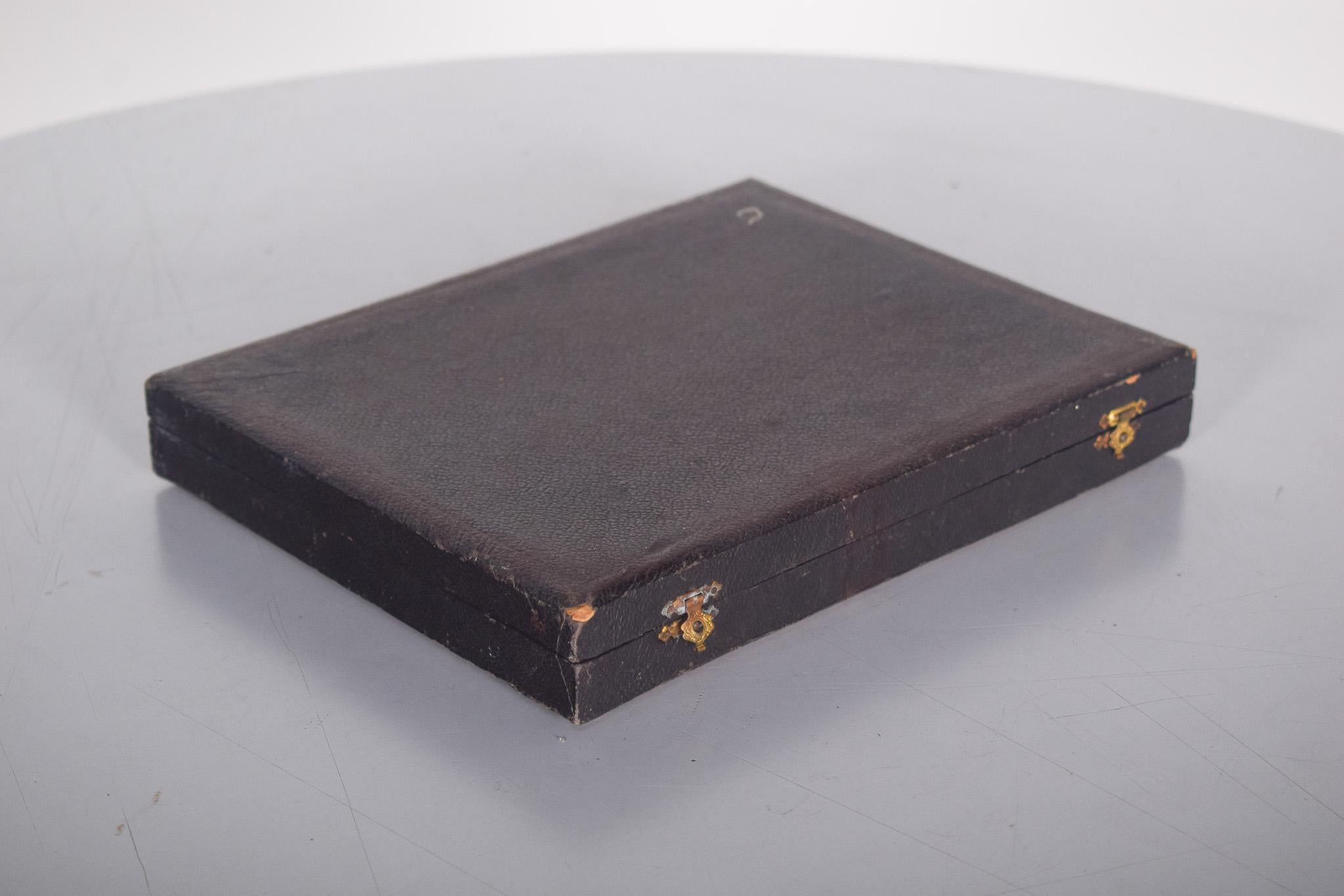 Boîte à couteaux, anglais. Contient un ensemble de 12 couteaux méticuleusement disposés. L'étui est rectangulaire, doublé à l'extérieur de similicuir noir texturé et doté d'un fermoir en métal doré, qui apporte une touche sophistiquée. A
