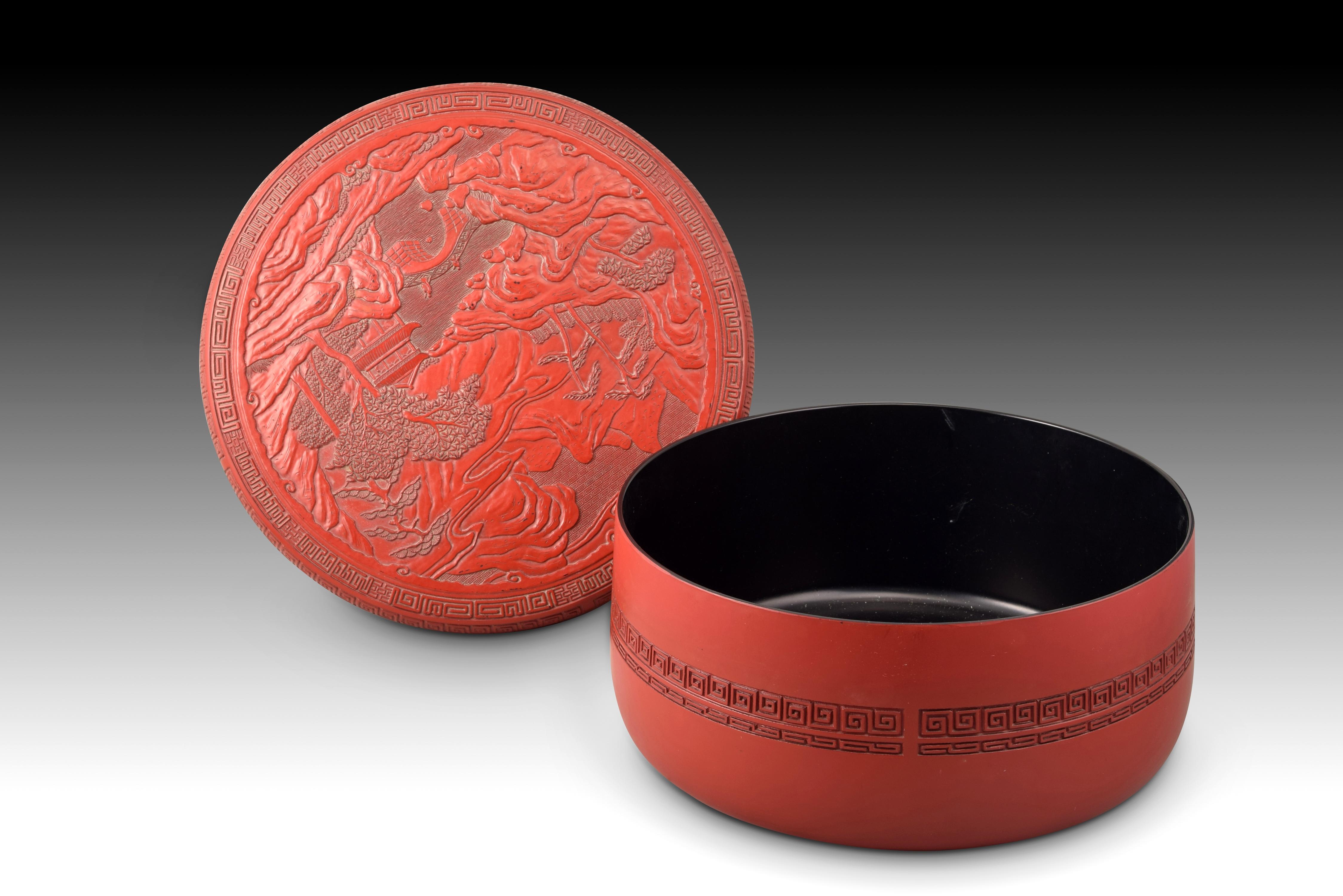 Box with landscape. red and black material. Possibly China, 20th century. 
Low cylindrical box with a flat lid that is red on the outside and black on the inside, decorated on the lid and the upper part of the body with bands of geometric and