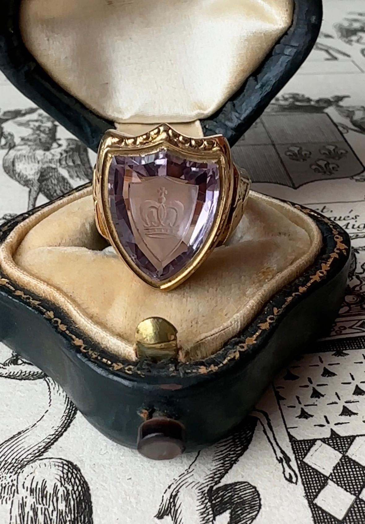 This glowing late Victorian ring is set with a luminous purple shield-cut amethyst that has been intaglio carved with a tiny crown. Substantially crafted in 12.2 grams of 18k gold, the shoulders are artfully adorned with hand-engraved fleur-de-lis