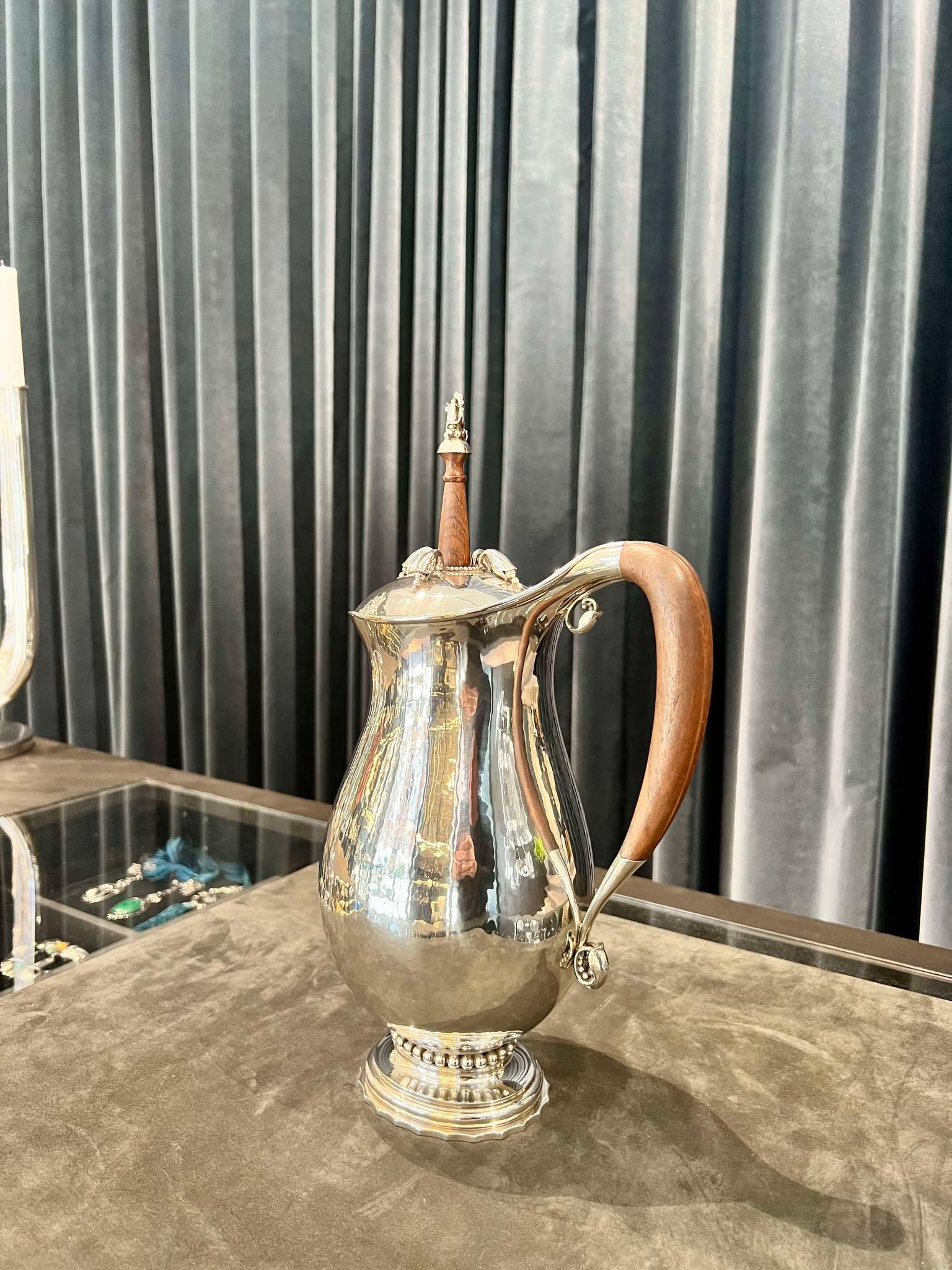 Georg Jensen sterling silver chocolate pot with a mahogany handle and a silver mounted rosewood stirrer, design #460B by Georg Jensen from 1925.

 Gross weight of the pitcher alone including the handle circa 450z (1,300g).
• This pitcher comes in an