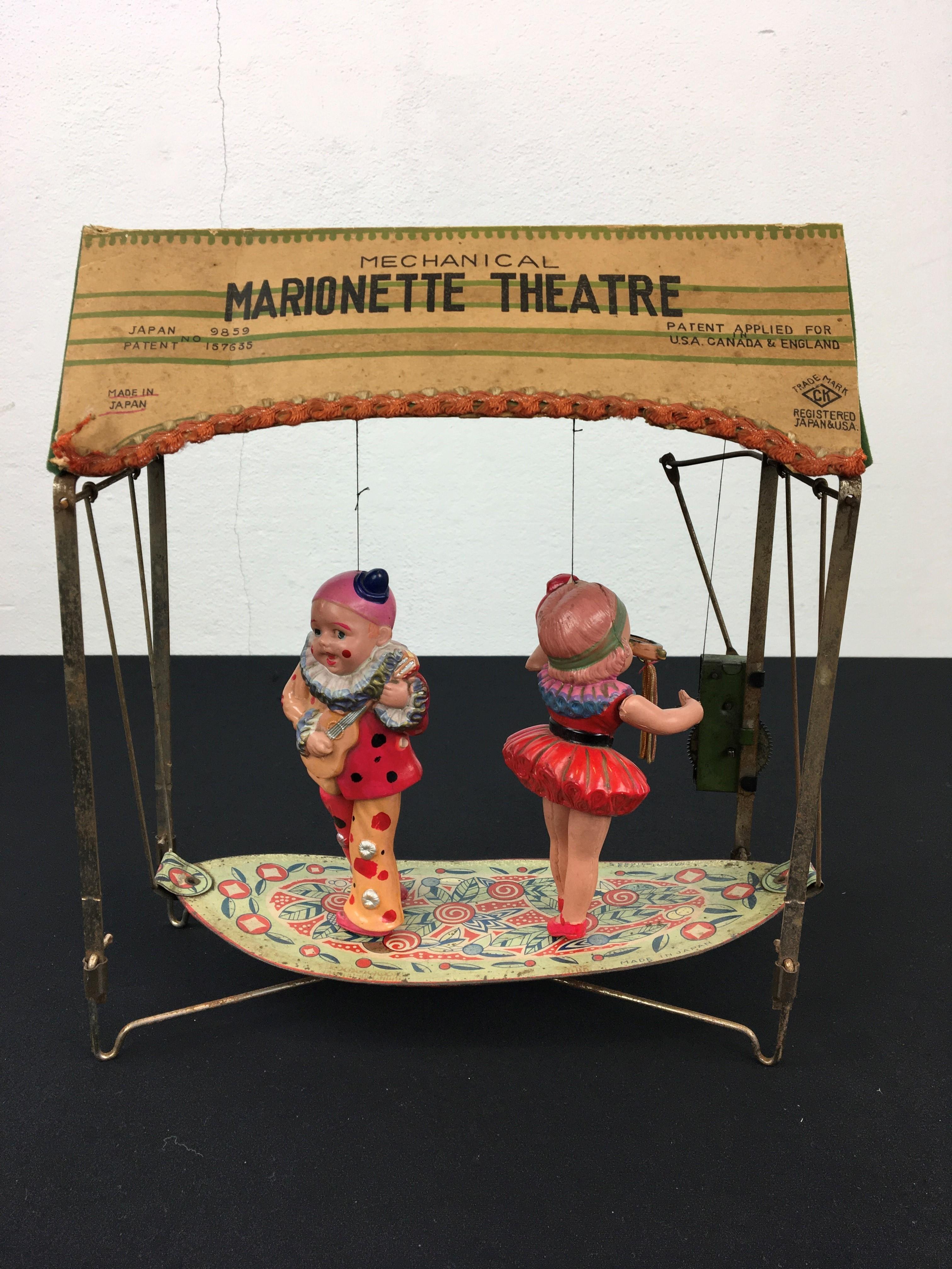 Antique mechanical marionette theatre toy by CK made in Japan. 
A clockwork tin - metal swing with 2 adorable celluloid puppets or dolls: a clown and a ballerina.
By the movement of the swing it seems that the boy and girl are dancing. 
At the back