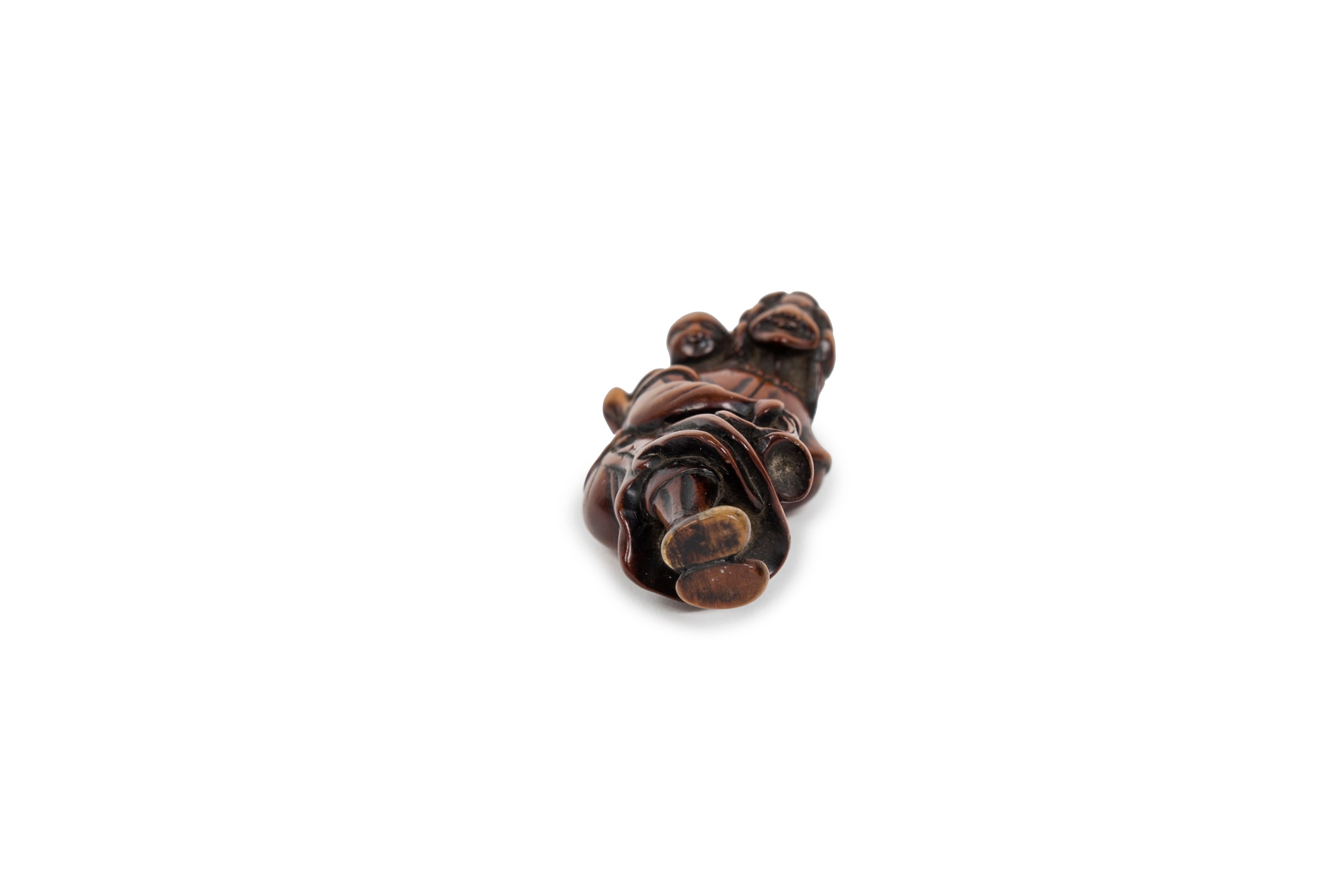 Wooden netsuke of a standing Dutchman figure with his mouth open, leaning forward. He is wearing a long curly wig, a ruff and a long coat tied at the waist. In his right hand, the man holds a trumpet decorated with two tassels, while his left hand