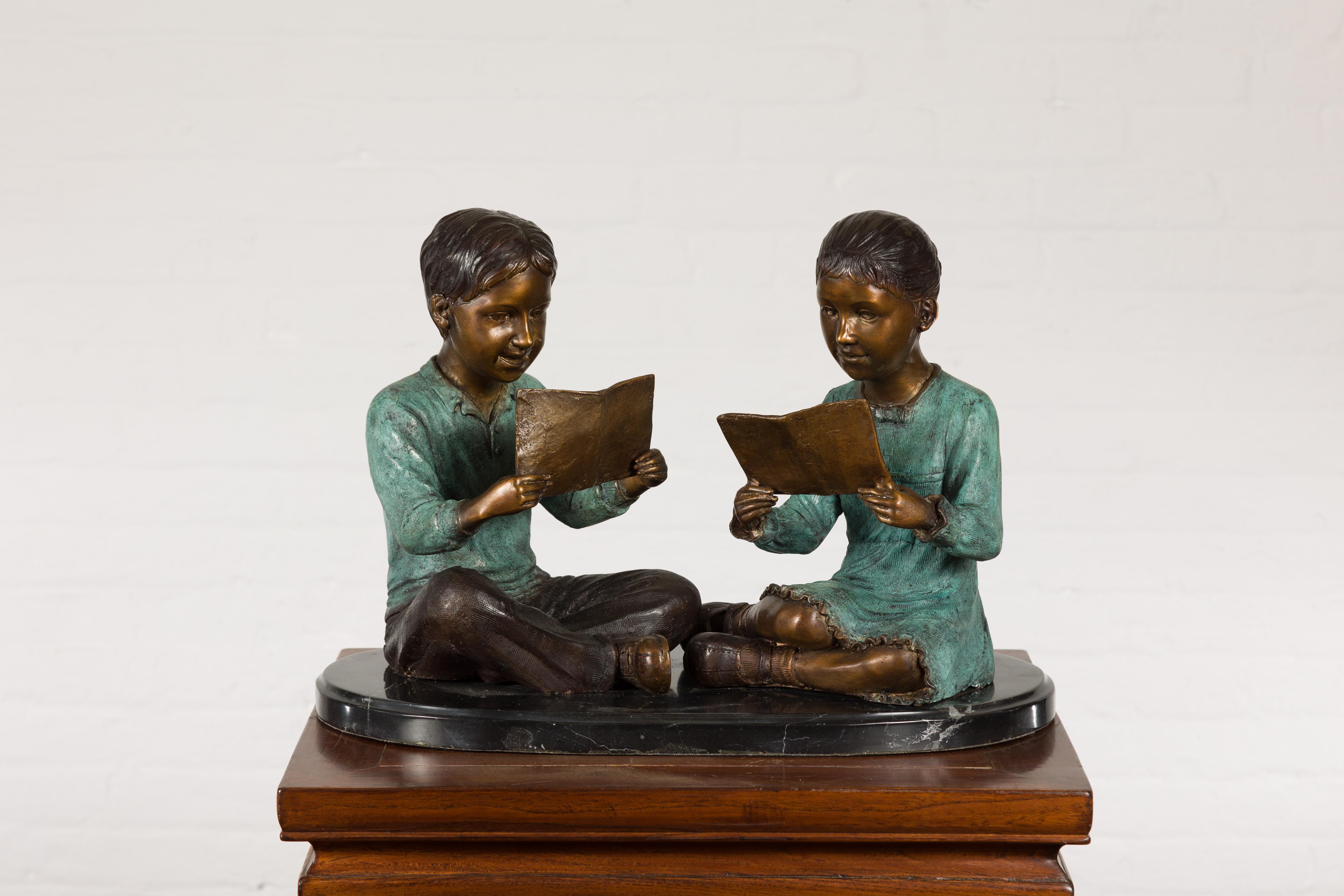 Junge und Mädchen lesen ein Buch, zeitgenössische Bronzeskulptur auf schwarzem Marmorsockel. Es handelt sich um eine laufende Produktion mit einer Vorlaufzeit von 19 bis 20 Wochen. Feiern Sie die Freude an der Geschwisterschaft und die Schönheit des