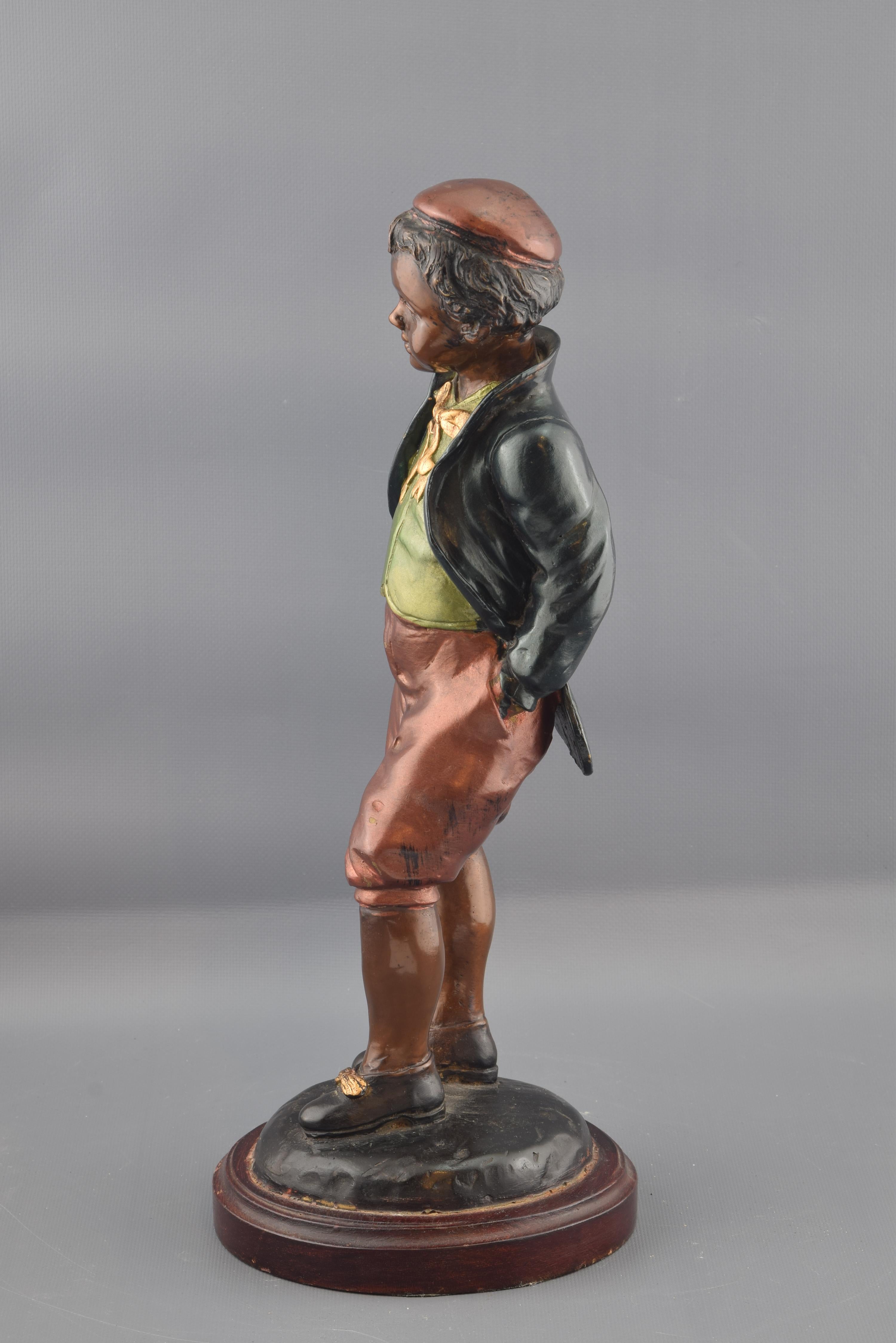 Figura in bronzo con finitura policroma posta su una base circolare che mostra un bambino vestito in modo umile. L'opera richiama opere europee (Francia, Vienna...) della fine dell'Ottocento o dell'inizio del Novecento sia per il materiale scelto