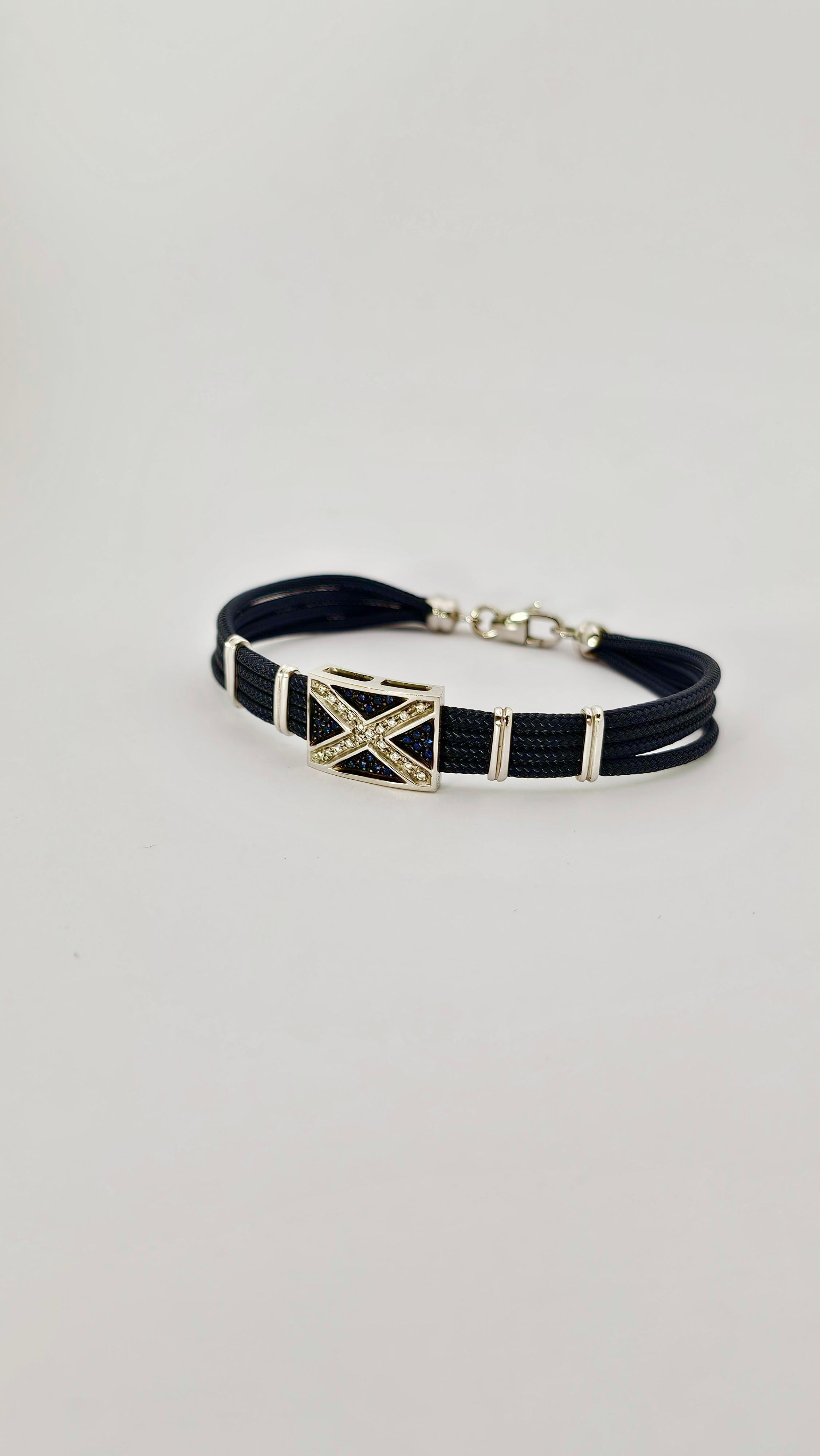 Una moderna pulsera de estilo náutico realizada en oro de 18 quilates.
El peso del oro es de gr. 9,30.
La parte del brazalete se compone de tres hilos superpuestos de sagola (alambre de barco) alineados mediante cuatro barras de oro blanco.
La