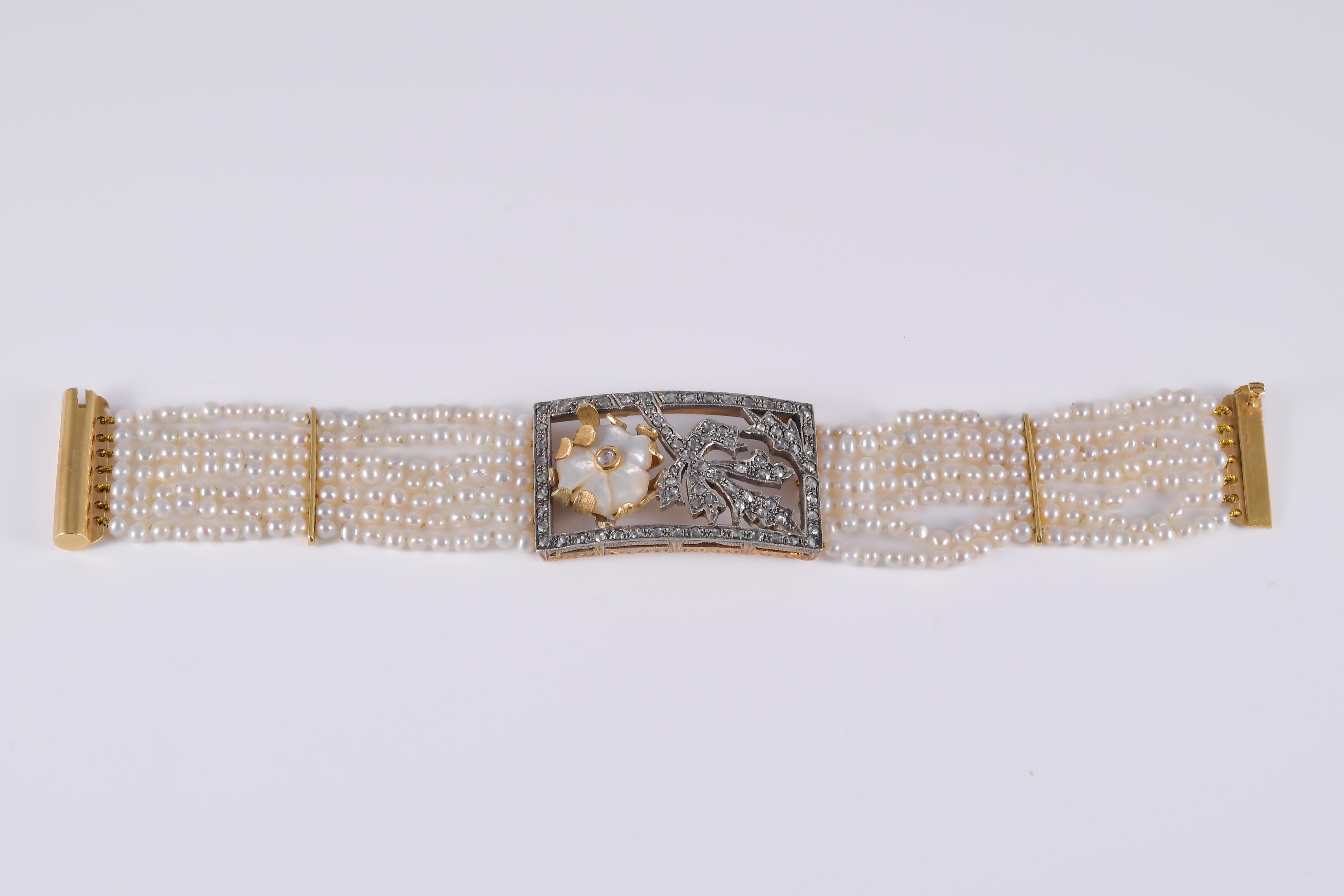 Bracelet en or blanc et jaune 18k (750/1000) et argent 14k 585/1000, composé de sept rangs de petites perles et centré par une grande formule rectangulaire décorée de bas-relief de nacre et de roses de diamants.
le poids total est de 45,18