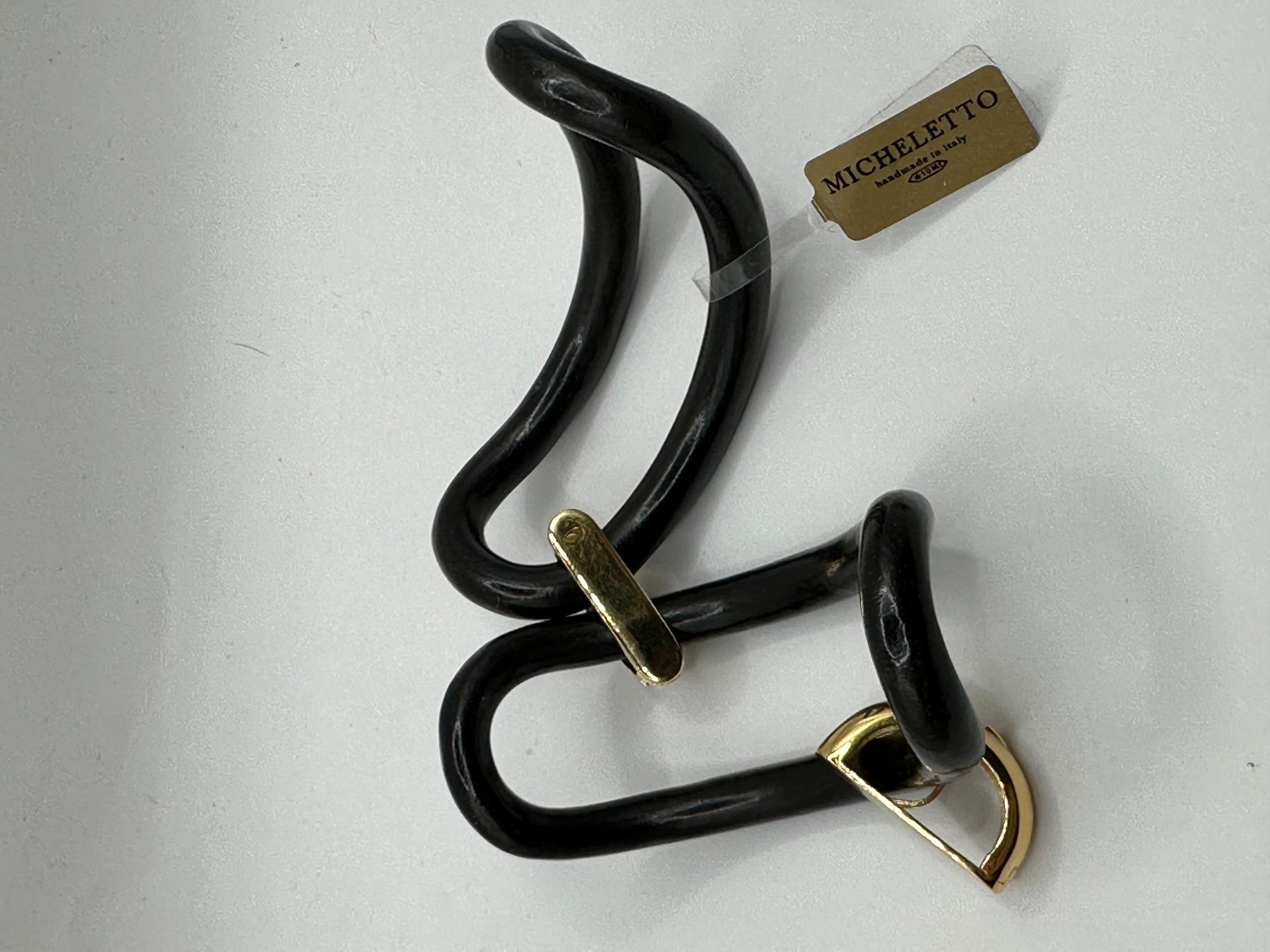 Un gioiello contemporaneo dal carattere deciso, questo bracciale è una vera scultura da indossare. Realizzato in ebano lucido, dalle superfici sinuose e profonde, è impreziosito da cavallotti in argento elegantemente placcati in oro 18kt. Il