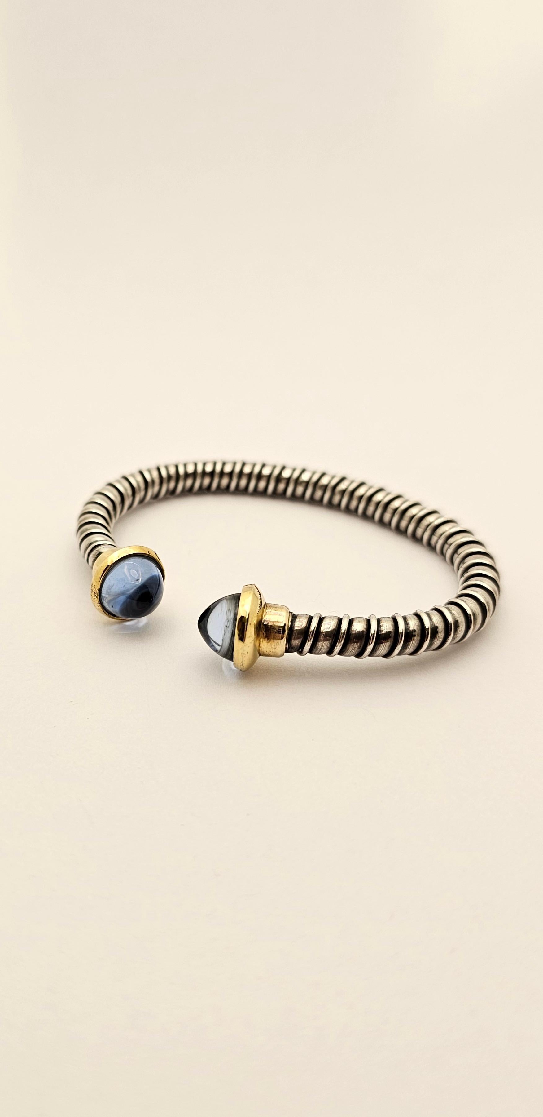 A 1990s semi-rigid bracelet made of silver tubogas mesh.
The two end pieces of the bracelet are 18 kt yellow gold in which are set two sugar loaf-cut blue Topazes.
This bracelet has a beautiful color combination, typical of 1990s design.
Its