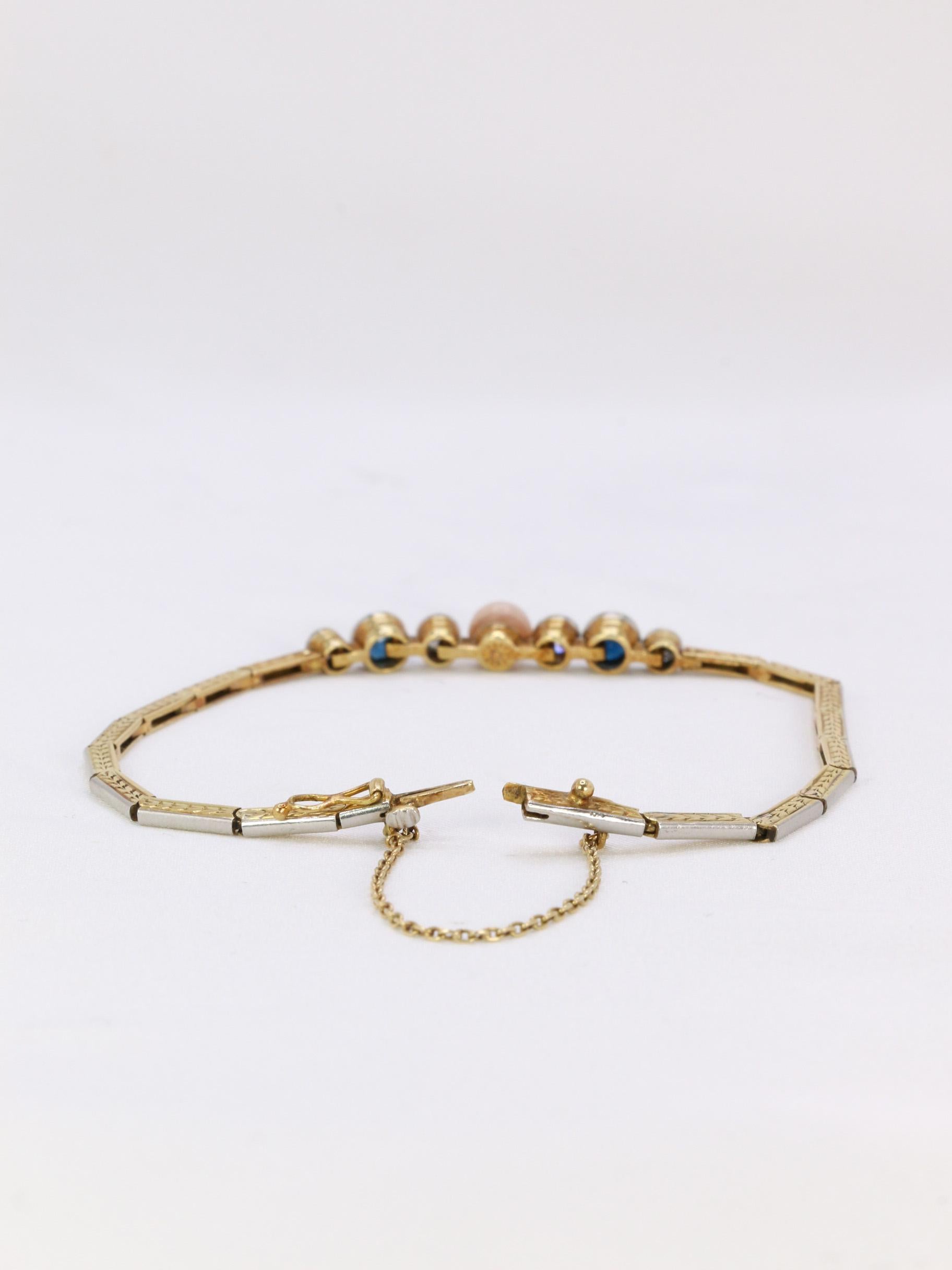 Bracelet en or 18k (750°/°°) composé d'un motif central comportant une perle fine bouton rosée, quatre diamants taille ancienne pour un poids total d'environ 0,4 carats et deux saphirs pour un poids d'environ 0,5 carats. Le bracelet articulé est