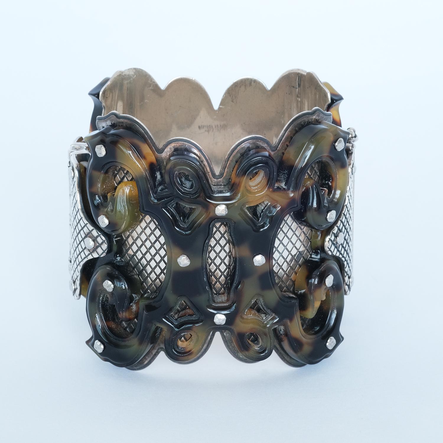 La base de este brazalete es de plata de ley, y sobre la plata hay una hermosa capa de acrílico marrón, formada en un antiguo estilo gótico. El dibujo acrílico también se complementa muy bien con los clavos metálicos que sujetan el acrílico a la