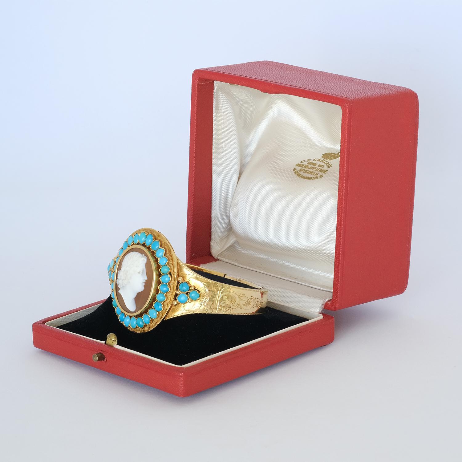 This 18 karat gold bangle has a beautiful cameo made out of shell and around the cameo there are 33 cabochon cut turquoises. The gold bangle itself is adorned with classic rocaille engravings.

This bangle fits the classic summer-dress as well as