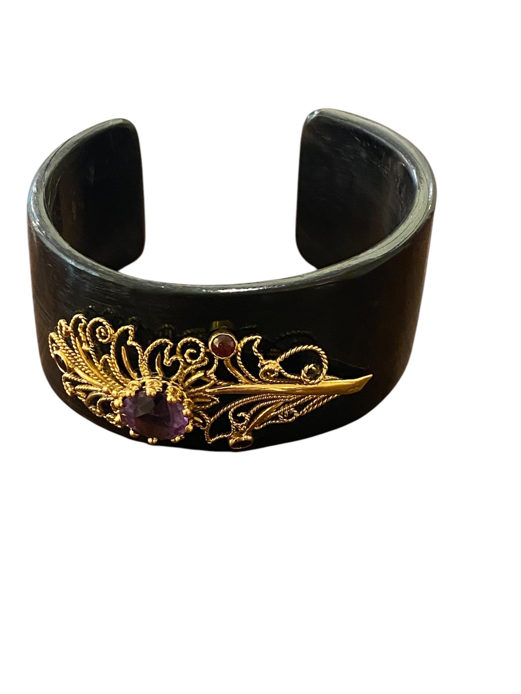 
Bracelet avec application en or jaune 19.2kt- 800‰. Le bracelet est large et rigide, en matière Horn d'un ton noir profond, avec une ouverture à l'arrière. La finition naturelle révèle les nuances subtiles et les motifs organiques caractéristiques
