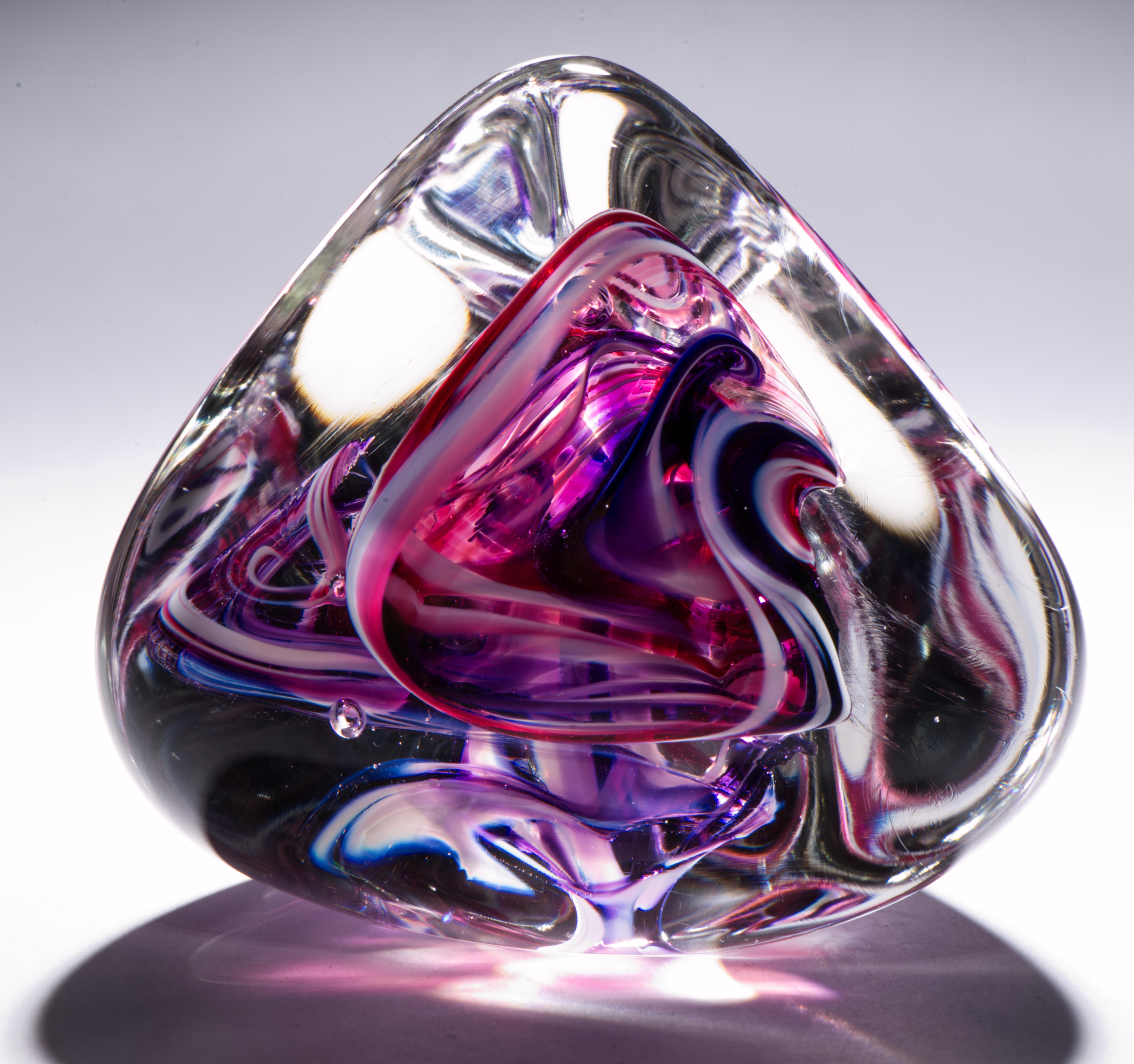  Die auffällige piramidale Skulptur oder der Briefbeschwerer hat ein abstraktes rotes und weißes Glasdesign, das von klarem Glas umhüllt ist; kontrollierte Blasen, die zwischen den frei fließenden farbigen Glaswirbeln verteilt sind, lenken das Auge