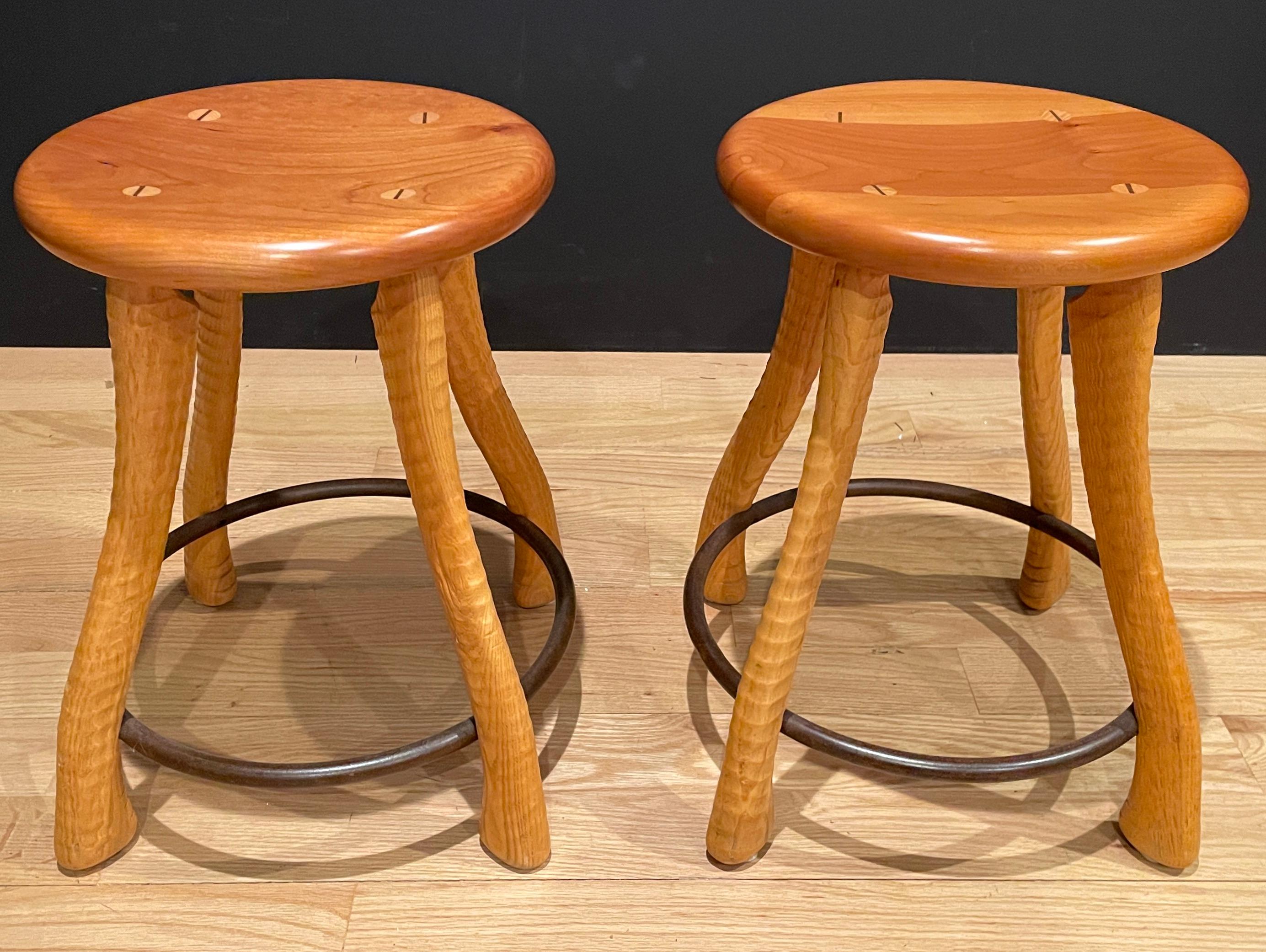 Uniquely designed wood and iron stools. Farmhouse country style with ax handle form legs supported by through dowels and iron ring. Designed and bench made by Bradford Woodworking of Worcester, Pennsylvania. 
Seat Diameter 13