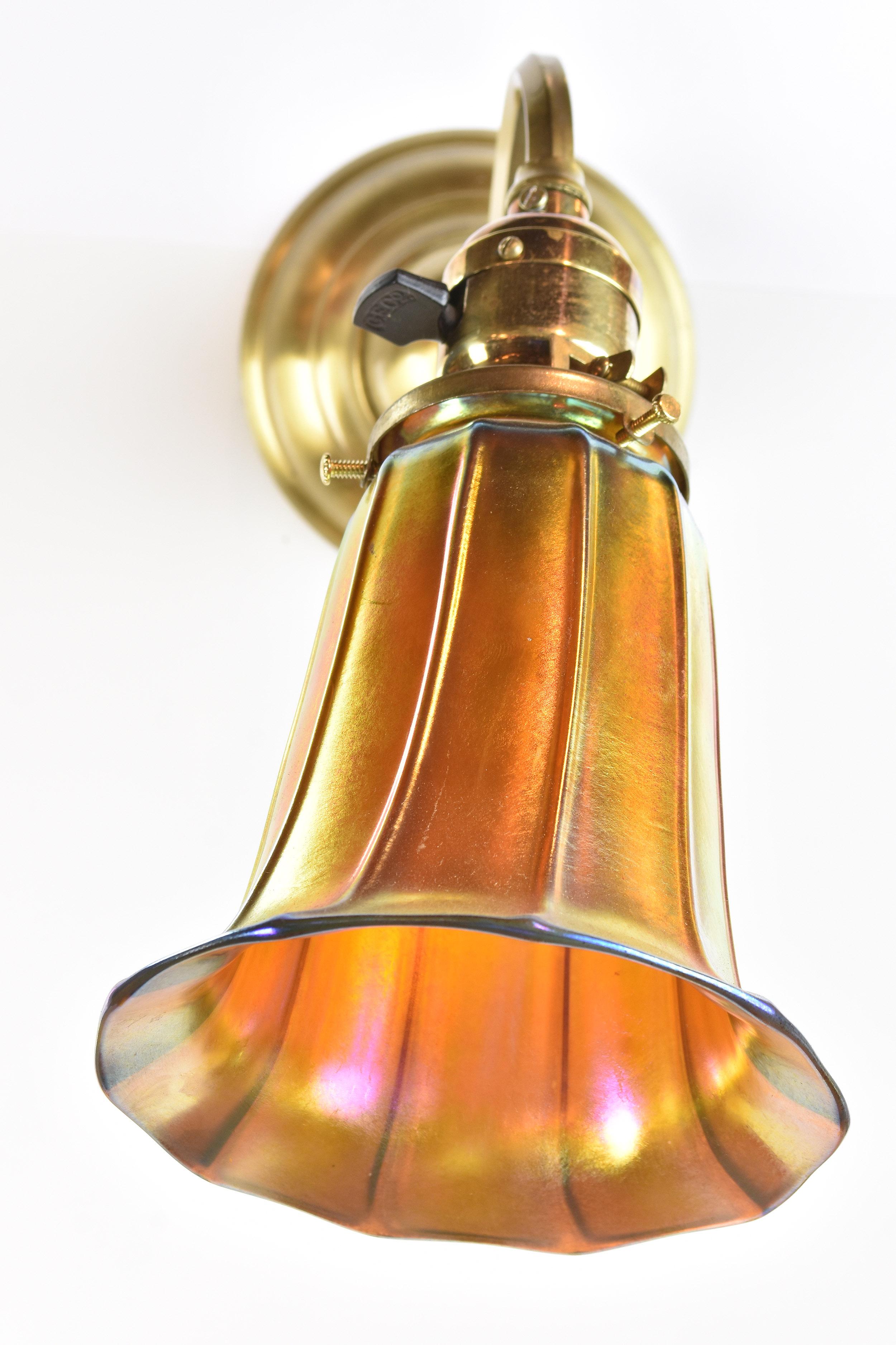 Three available.

This striking sconce was manufactured by Bradley & Hubbard, a premier lighting company of the late 19th and early 20th century. The golden hardware compliments the orange hue of the shade, which reflects light
