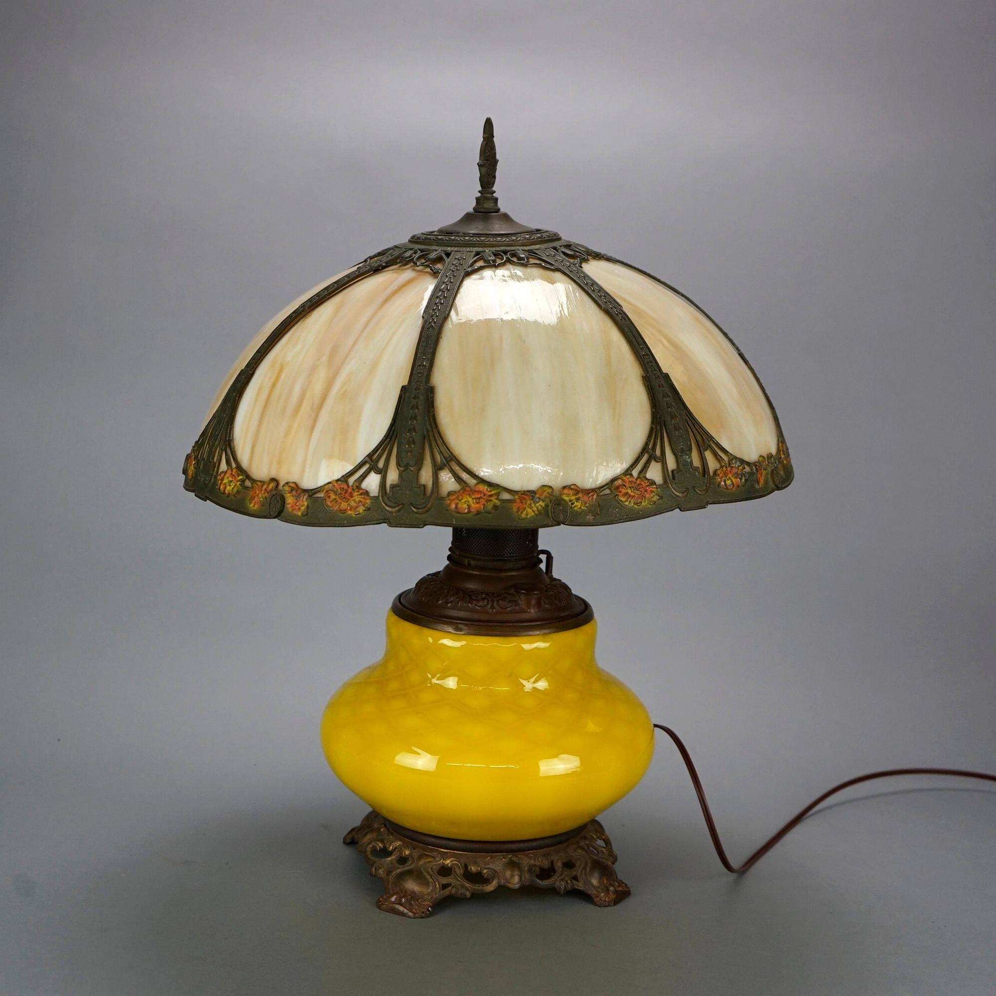 An antique Arts and Crafts table lamp in the manner of Bradley and Hubbard offers polychrome dome form cast shade housing slag glass panels over single socket lemon quilt art glass base, c1910.

Measures- 22.5''H x 17.75''W x 17.75''D.