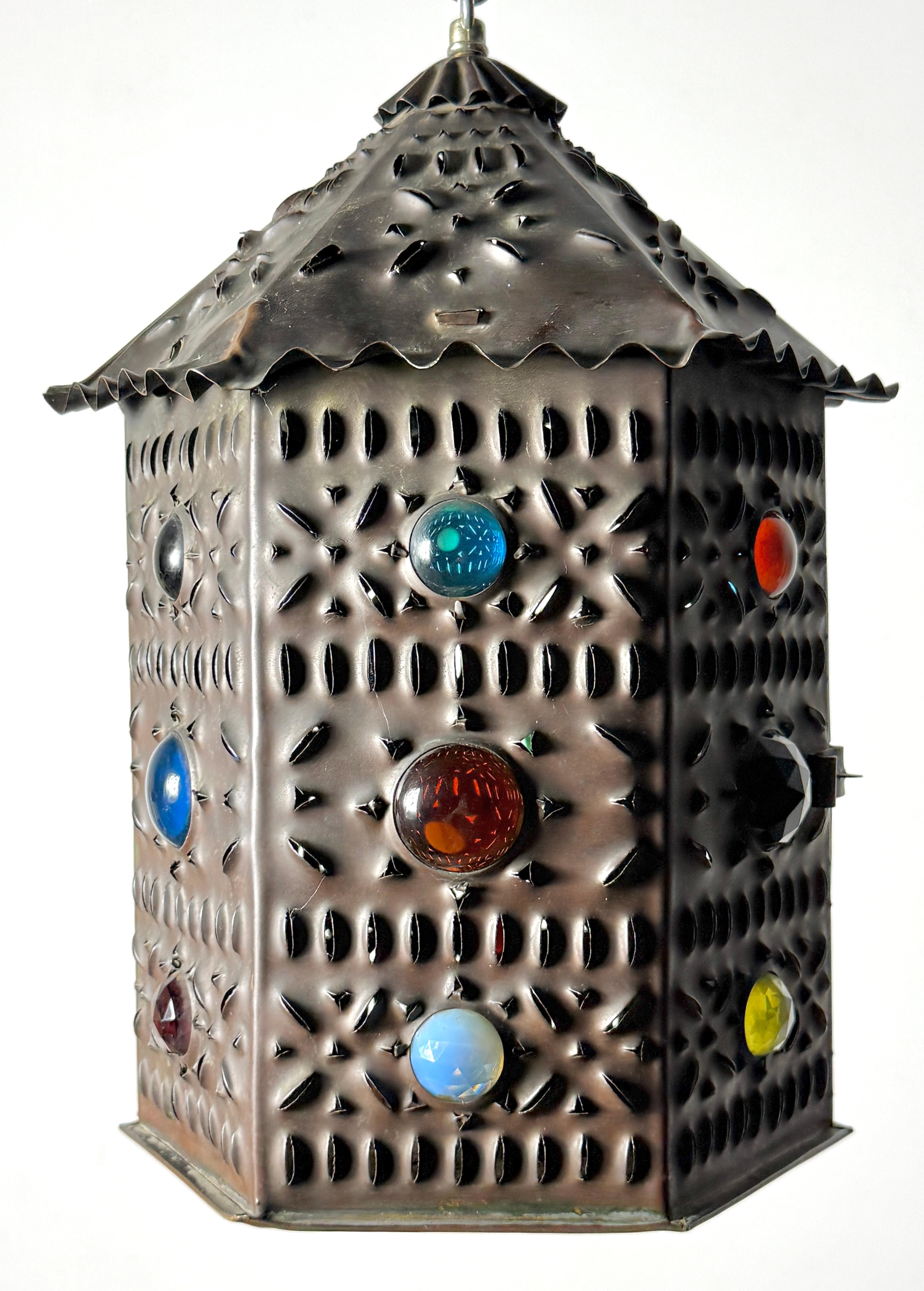 Farol colgante de latón punzonado con joyas, estilo Bradley & Hubbard
EE.UU. circa principios del siglo XX

Forma hexagonal de latón fino con detalles perforados y joyas multicolores incrustadas
La puerta abatible se abre para revelar el portavelas