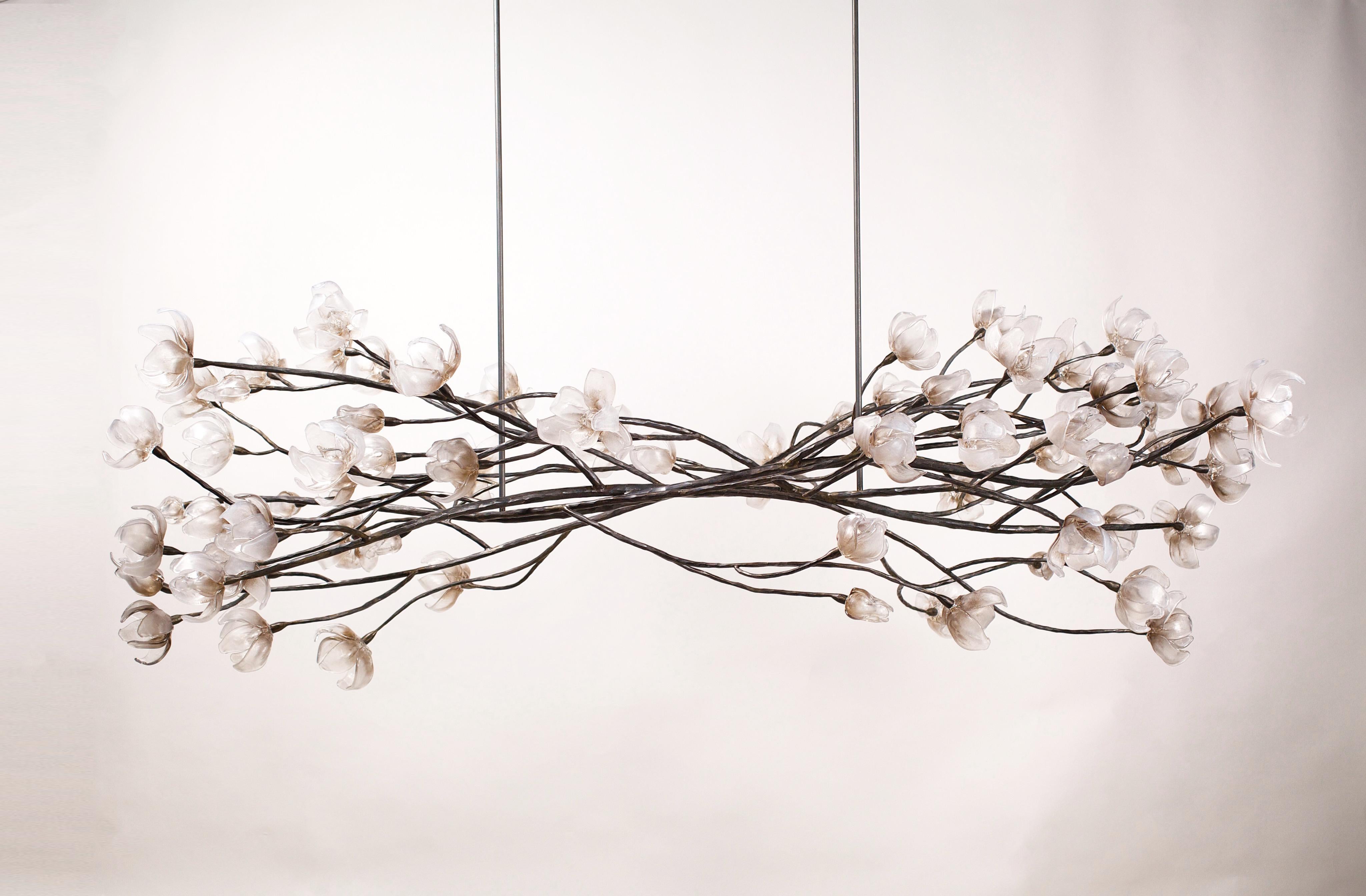 Branching Magnolia Series hanging sculpture by Elizabeth Lyons

Inspired by nature, seventy-five hand sculpted glass magnolia blossoms in various stages of opening adorn a structure of solid forged and welded steel branches. The branches have been