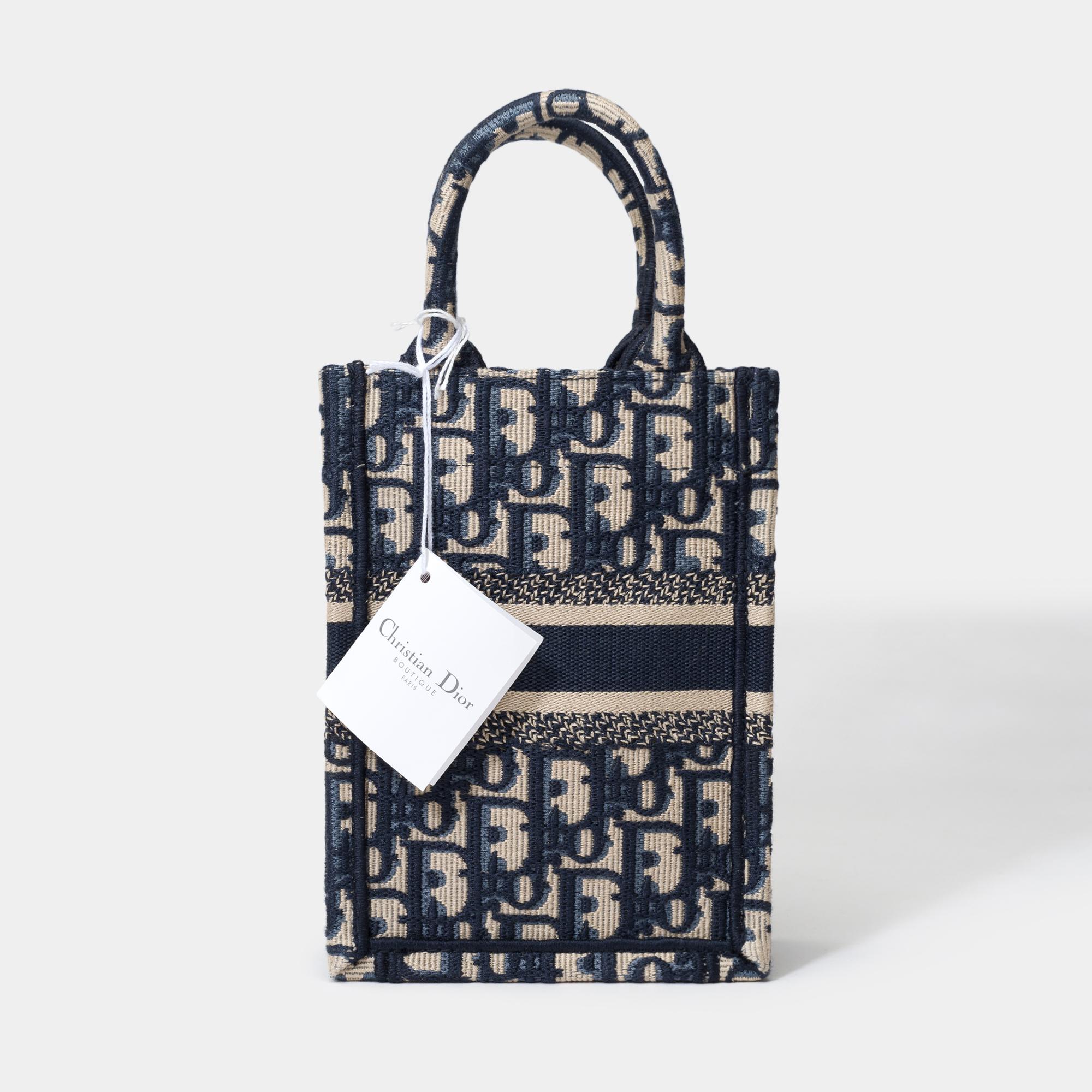 The​ ​vertical​ ​Tote​ ​bag​ ​enriches​ ​the​ ​iconic​ ​Dior​ ​Book​ ​Tote​ ​line.​ ​A​ ​perfect​ ​example​ ​of​ ​Dior​ ​craftsmanship,​ ​this​ ​model​ ​is​ ​entirely​ ​embroidered​ ​with​ ​the​ ​beige​ ​and​ ​navy​ ​canvas.​ ​Enhanced​ ​by​ ​the​