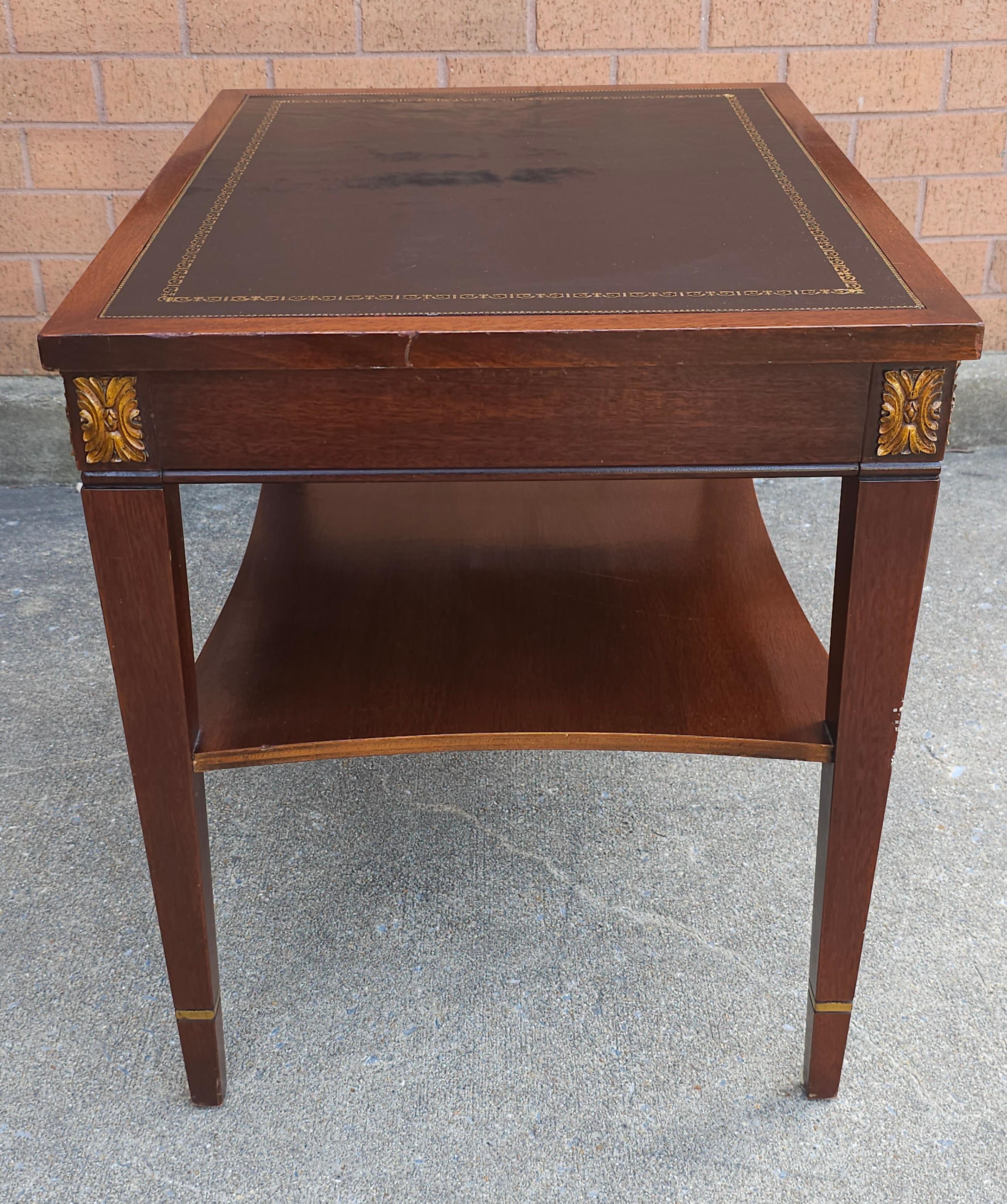 A Brandt Furniture Partial Gilt And Black Tooled Leather with gold stenciling Mahogany two Tiered Side Table
Measures 19.5