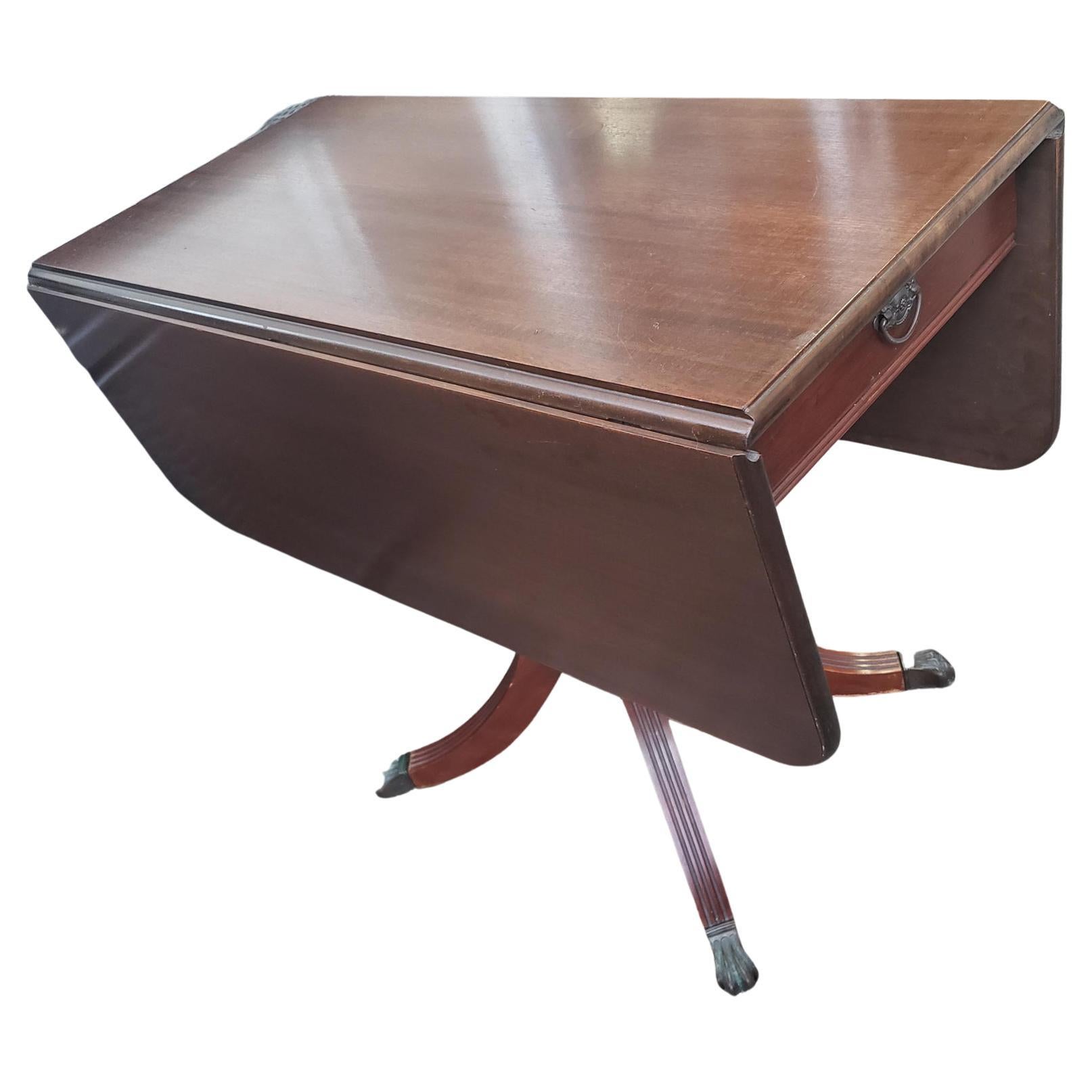 Prestigious Brandt furniture vintage dropleaf pedestal dining table. It features a sleek dovetail side drawer, a hand rubbed and polished semi-gloss finish. The Sheraton style pedestal has 4 fluted legs which terminate with antique brass lion paw