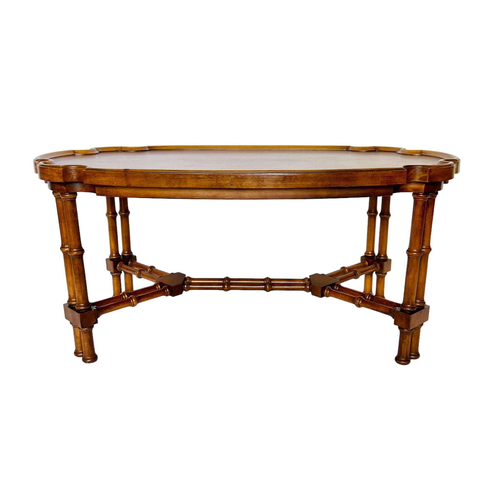A vintage Asian inspired Chippendale fruitwood cocktail table from Brandt's Embassy collection of the 1960s. It features an oval piecrust style scalloped top with lipped edge supported by banded faux bamboo double shafted legs and