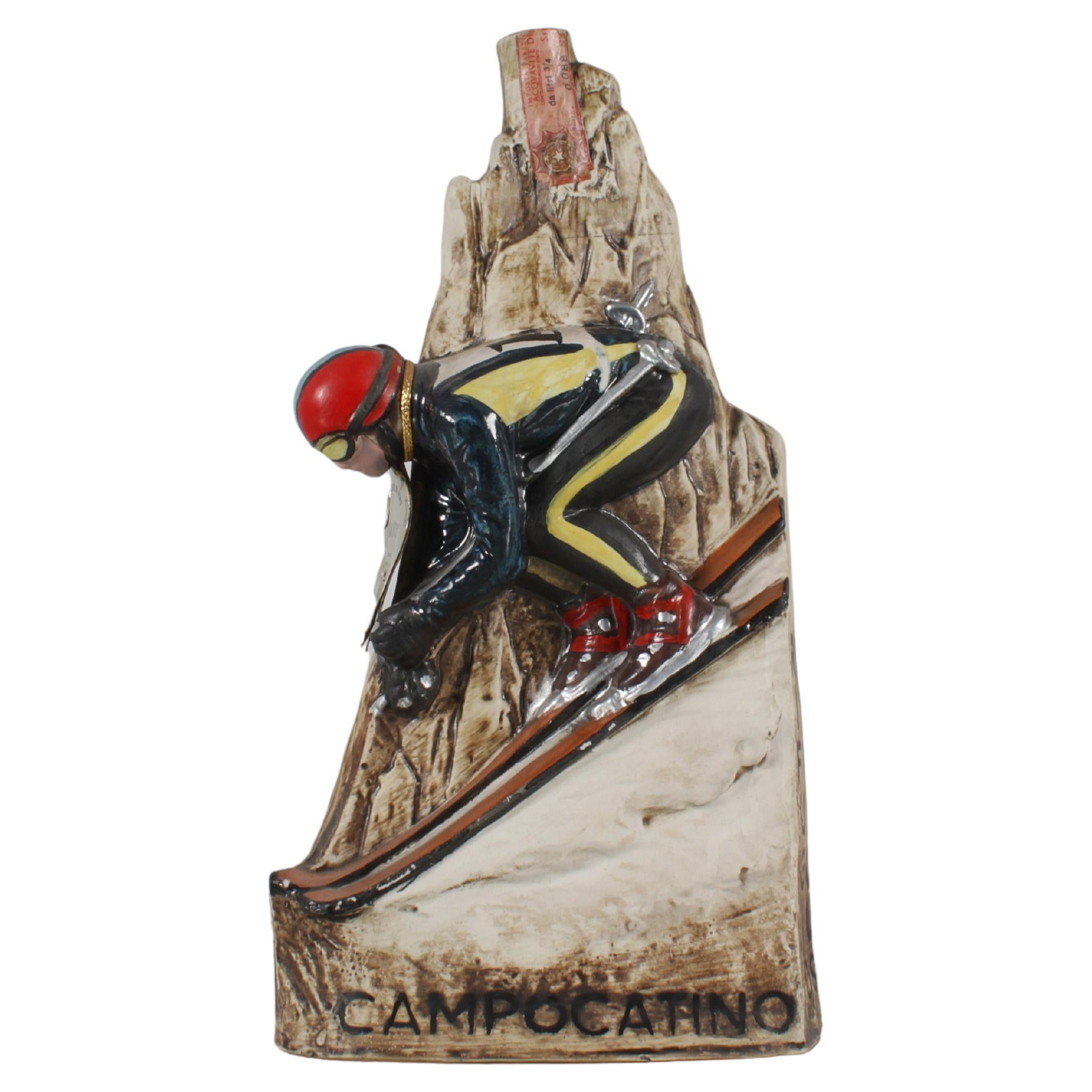 Seltene Flasche - handgefertigte und bemalte Werbeskulptur aus Keramik, die einen Skifahrer auf einem Berggipfel darstellt. Brandy - 
