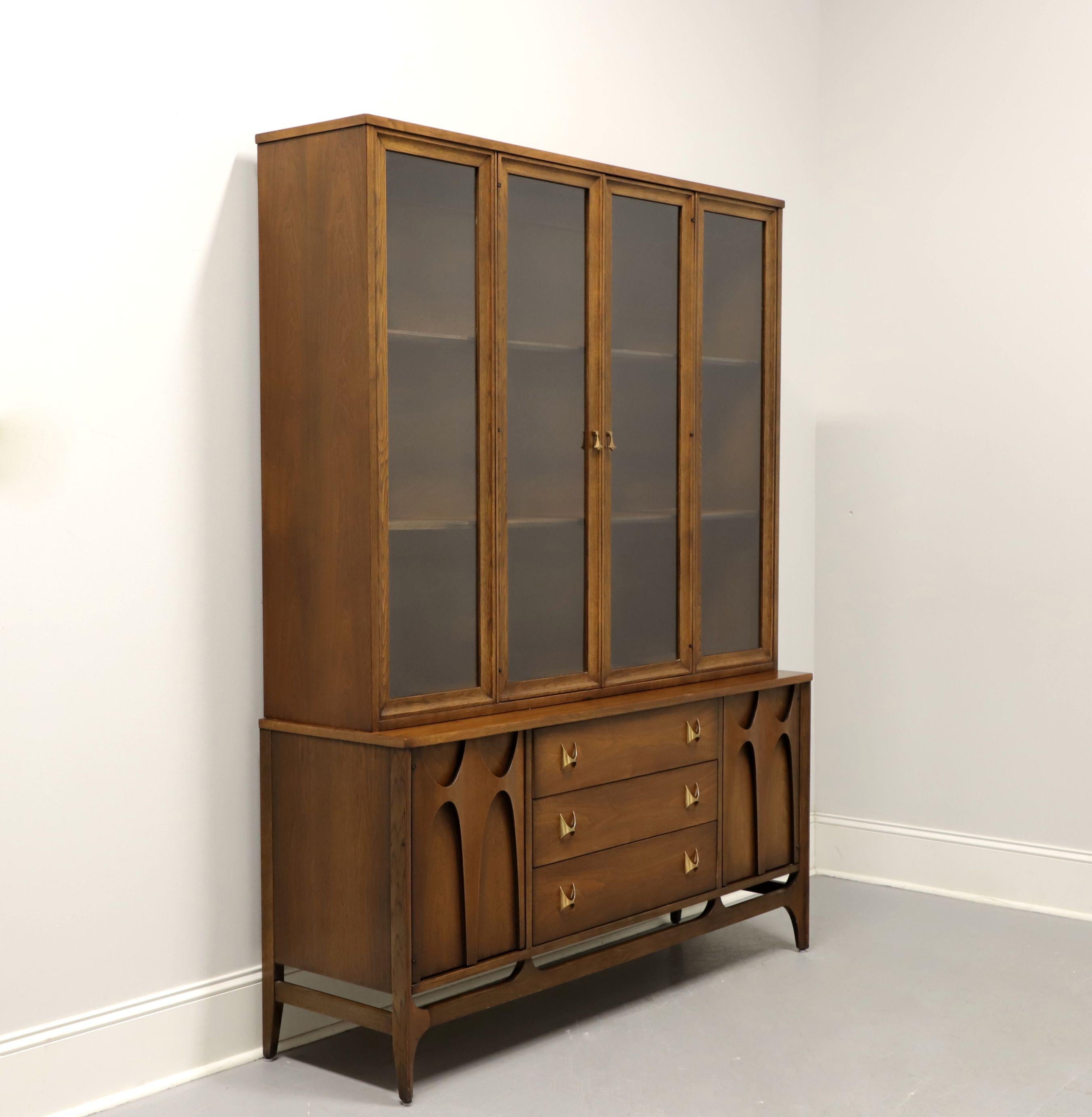 A Mid Century Modern china cabinet by Broyhill Premiere, from their Brasilia Collection. Walnut with brass hardware. Upper cabinet features two fixed plate grooved wood shelves behind dual glass doors with flanking glass panels. Lower cabinet