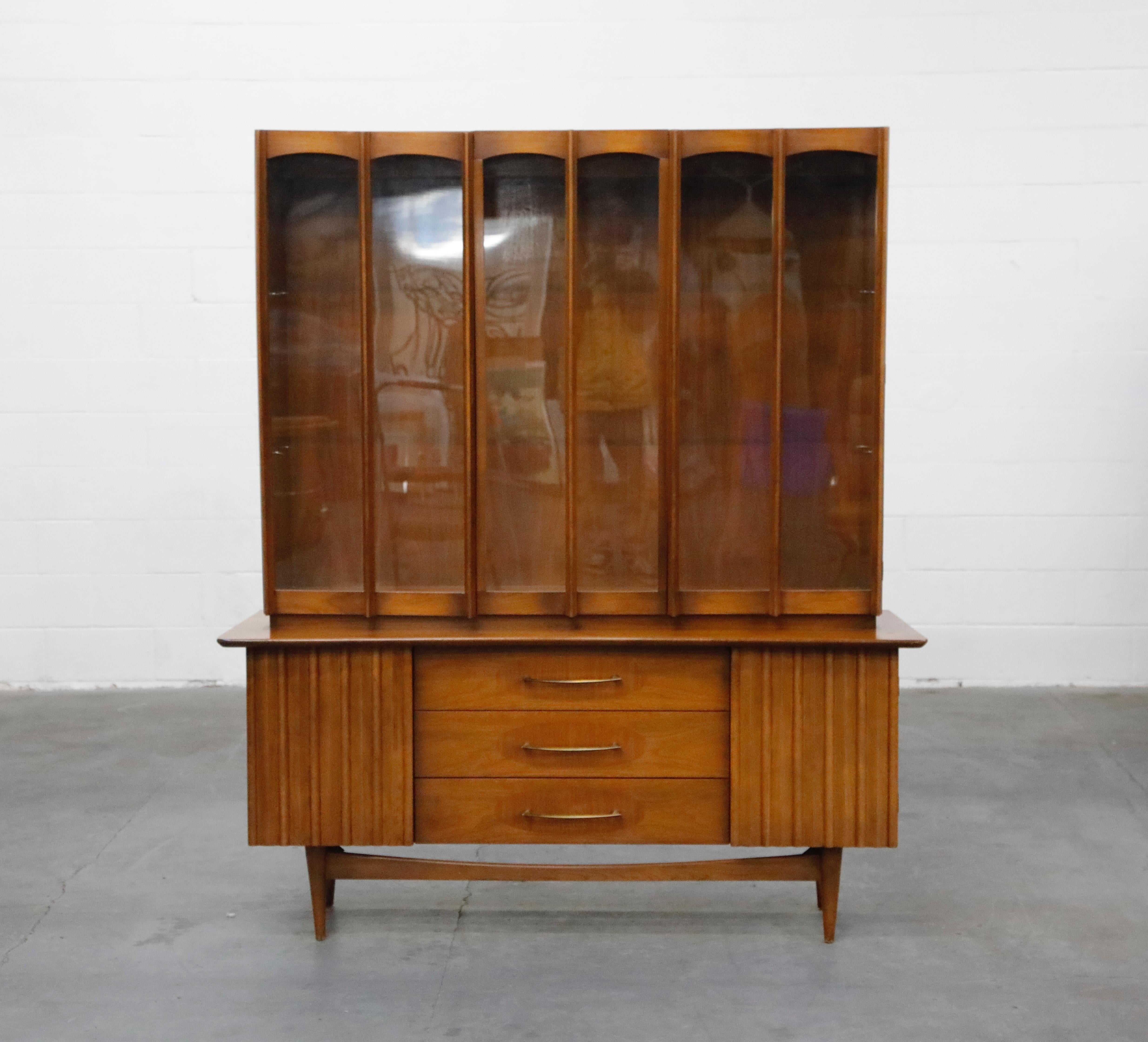 This large Brasilia styled American Modern sideboard credenza and hutch wall unit has beautiful midcentury details adorning its exterior and ample storage inside. The top china cabinet has two doors of glass and Brasilia styled slatted wood panels