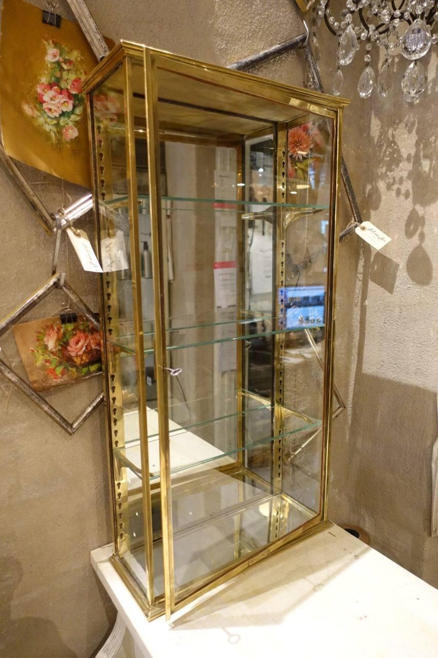 Magnifique vitrine ou armoire murale vintage en laiton français. Fourni avec une clé:: et trois étagères en verre:: ainsi que des supports muraux réglables en laiton moulé. Provenance - décor de boutique:: avec l'étiquette du producteur toujours en