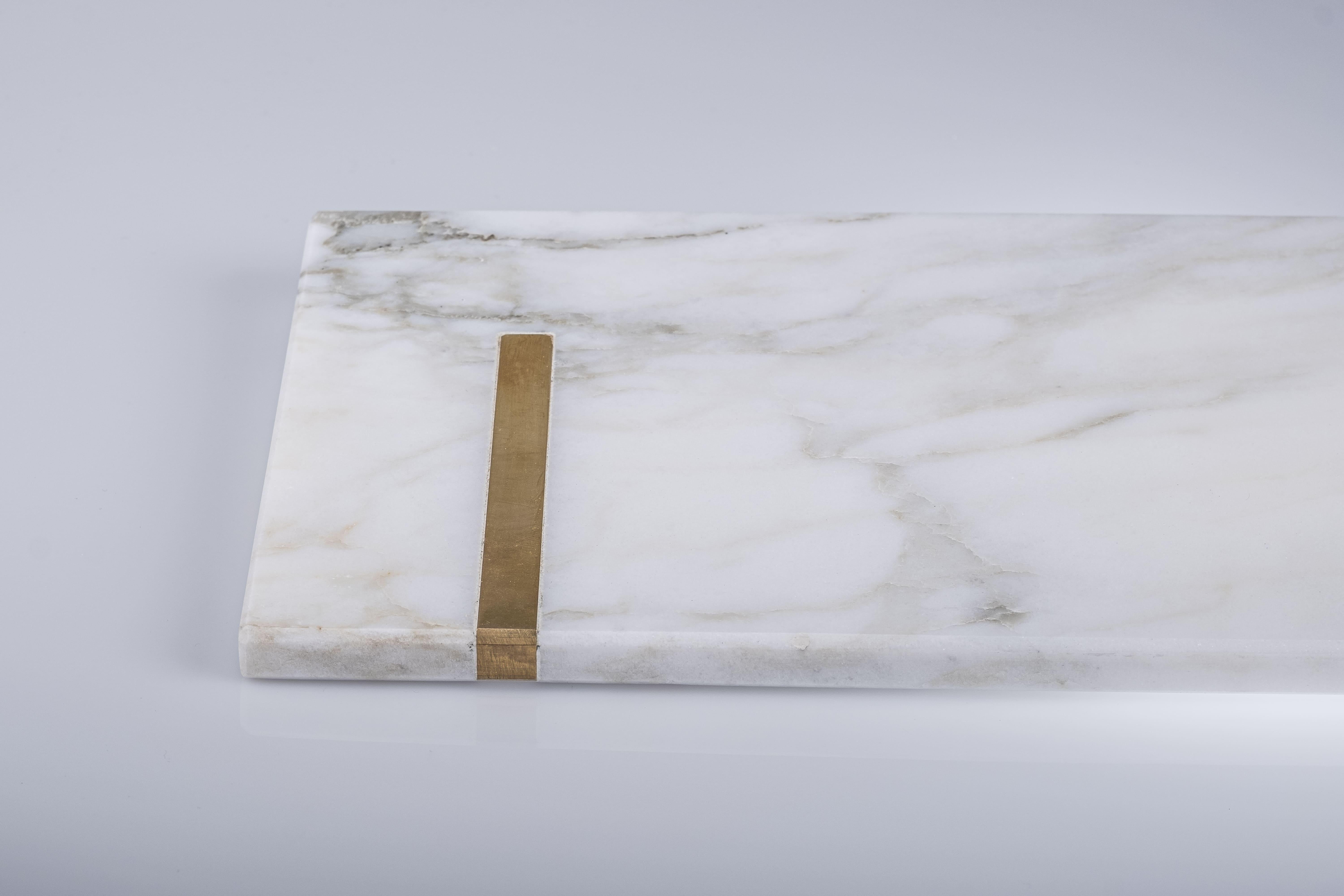 La planche à découper Brass, entièrement réalisée en marbre, est une planche à découper exclusive dotée d'une poignée rectangulaire en or Calacatta et d'une languette en laiton à l'une de ses extrémités, ce qui lui confère une touche supplémentaire