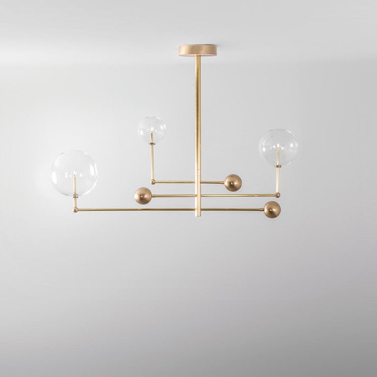 Brass 3 arm contemporary chandelier by Schwung 
Dimensions: D 25 x W 128.2 x H 178 cm 
Materials: solid brass, hand-blown glass globes
Finish: solid natural brass.
Also available in finishes: polished nickel or black gunmetal. 
All our lamps