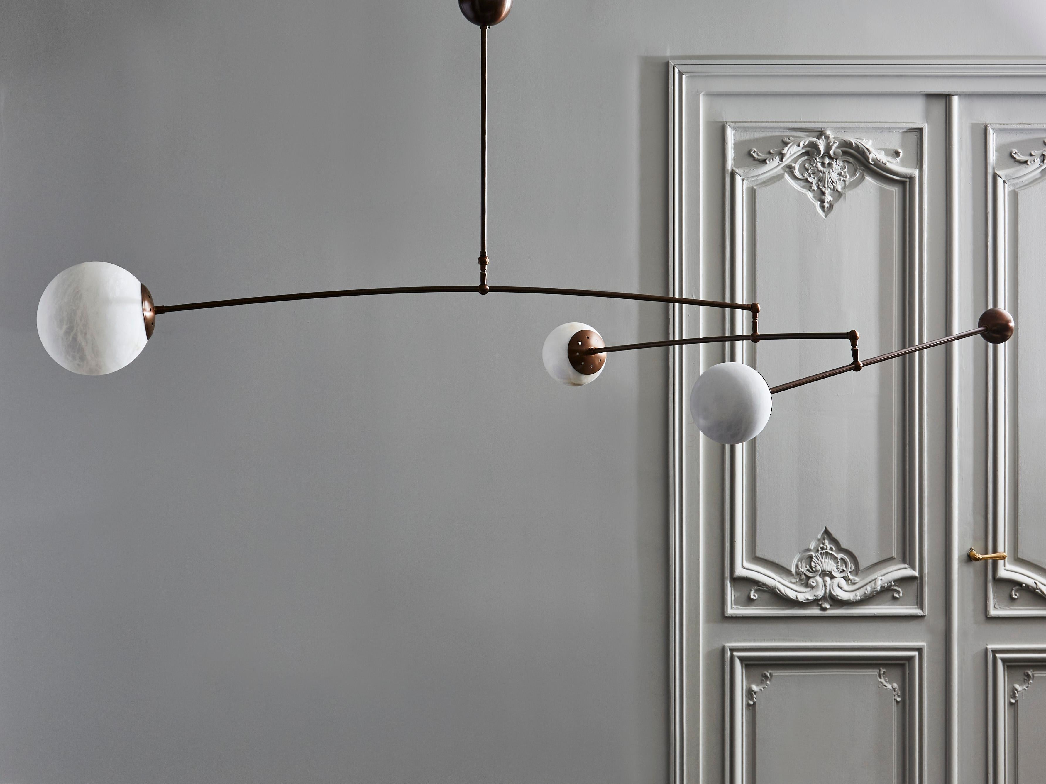 Mobile kinetic chandelier made of three patinated brass arms of light each holding different sized alabaster globes and counterweight to ensure the balance of the piece.

Original design by Glustin Luminaires.