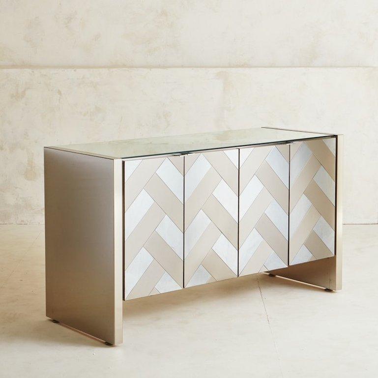A lovely brass and aluminum cabinet by Ello International. This cabinet features four brushed brass and brushed aluminum doors in a chevron design with chrome pulls. The doors open to reveal two adjustable shelves. It has an elegant mirrored top and