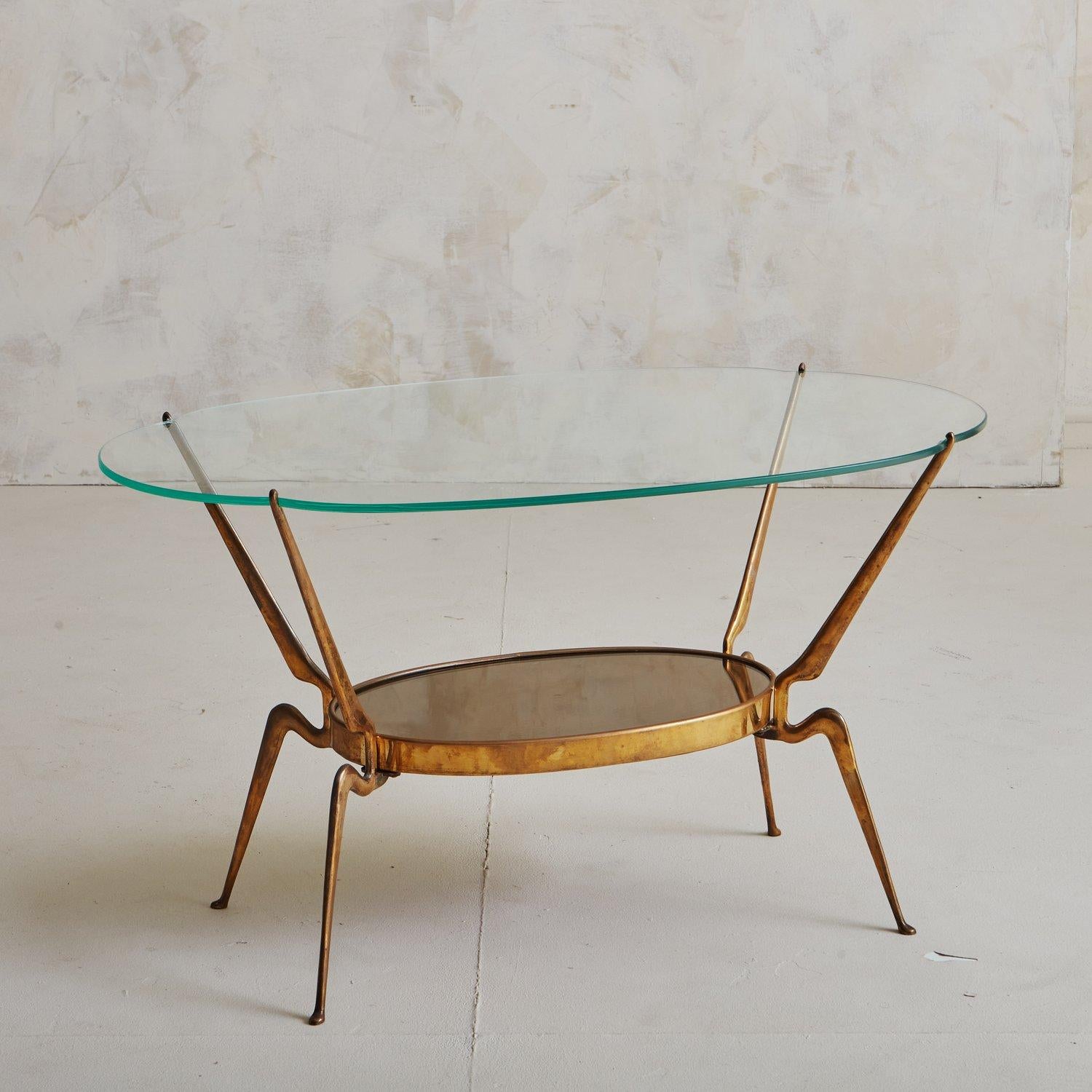 An elegant Italian coffee table featuring a sculptural brass base with a gorgeous patina and an oval back painted glass shelf. The base supports an oval glass top with subtle scalloped edges. Sourced in Italy, 1970s.

