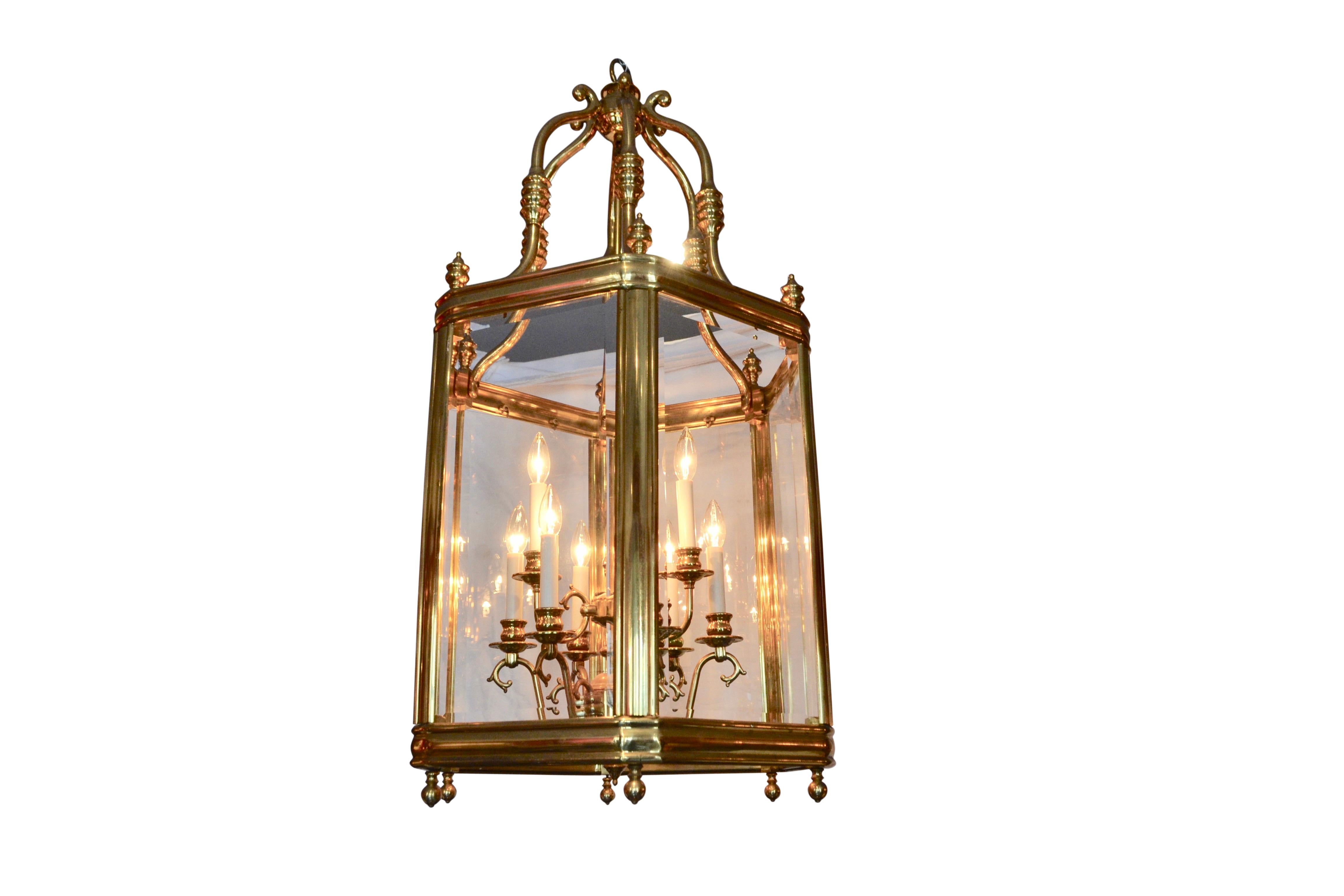 A contemporary brass and beveled glass hall or dining room lantern/chandelier with six rectangular beveled glass framed sides supported from the top to the canopy by six scrolling arms. A central brass rod supports nine interior decorative scrolling