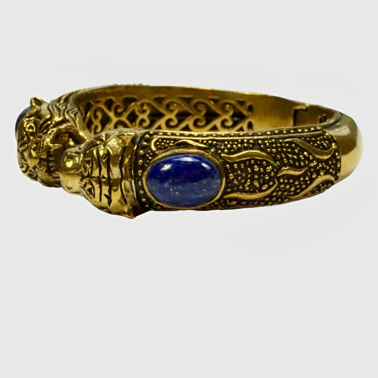 Splendido bracciale ornato in ottone e smalto nero, con due teste di tigre incastonate con pietre di lapislazzuli. Misura un diametro interno di 5,9 cm di lunghezza e una larghezza interna di 5 cm. La larghezza della parte anteriore è di 1,5 cm.

Si