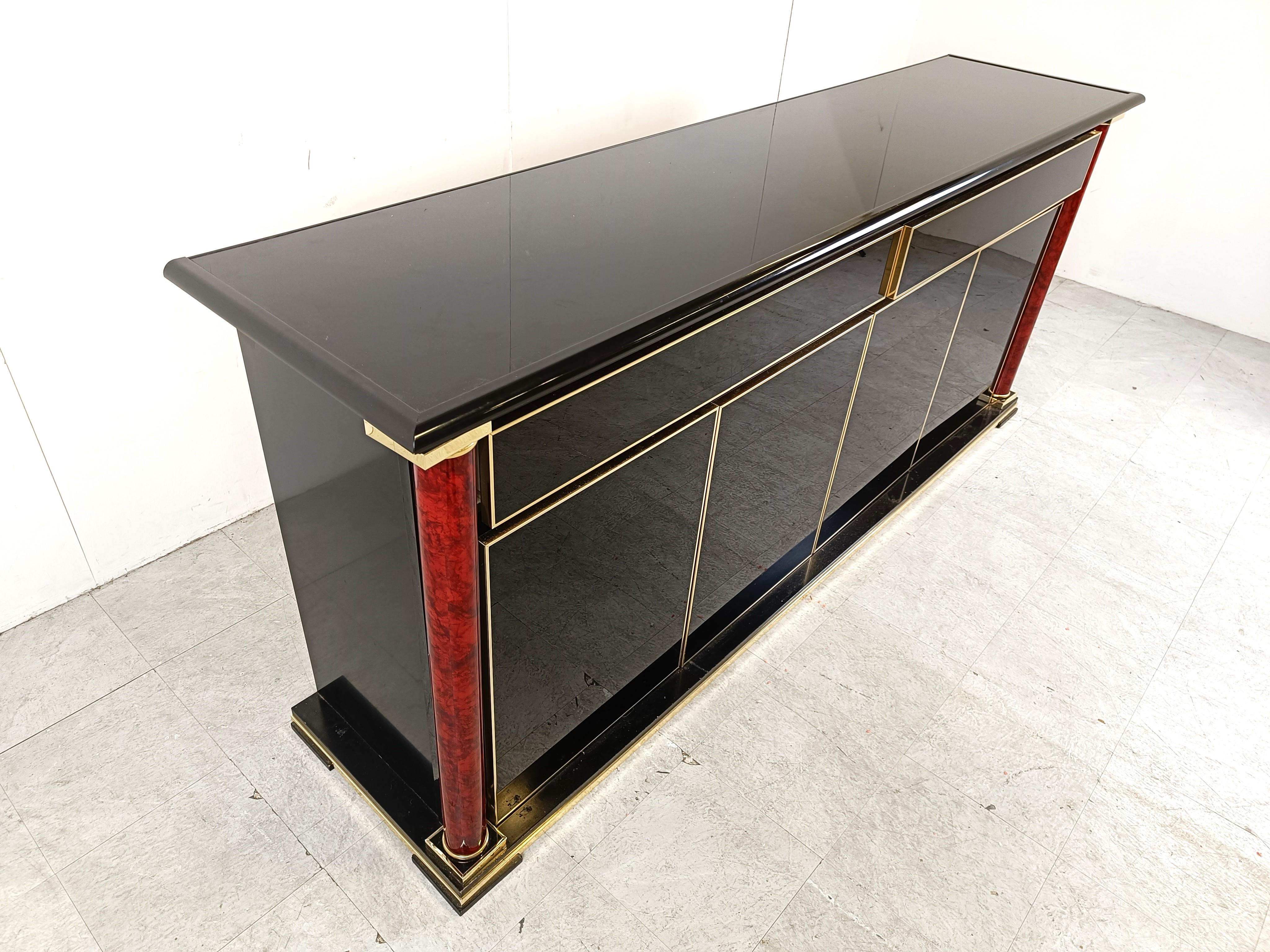 Luxurious seventies glamour sideboard made from black lacquer panels, brass decor and two wooden columns.

With 4 doors and 2 large drawers the sideboard offers plenty of storage space. 

The use of different high quality materials makes this piece