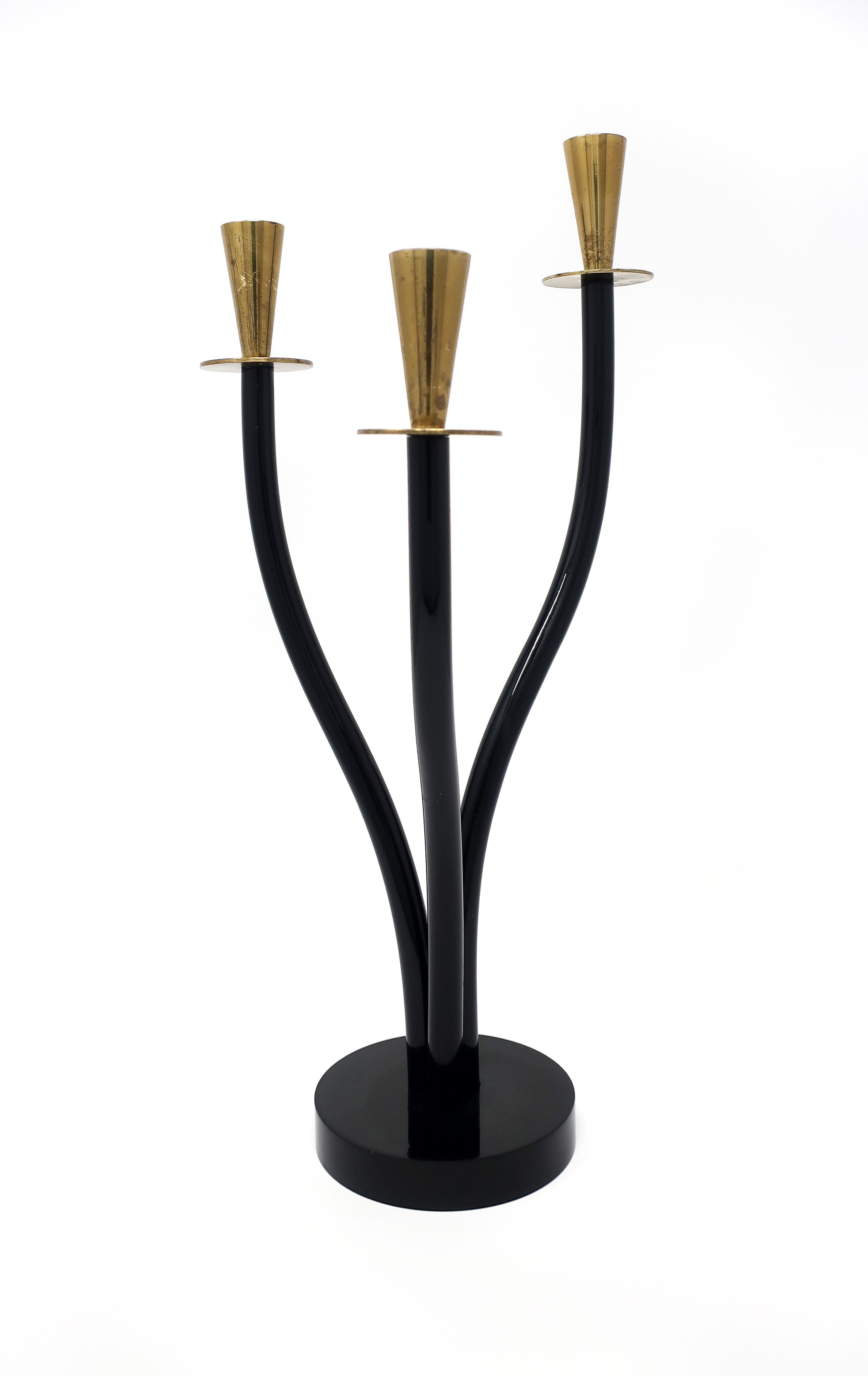 A vintage brass and black Lucite candleholder that screams Mid-Century Modern. Plantlike in form and reminiscent of a flower in bloom, the three curved stems, set into a round black acrylic base, each has a brass cup and saucer candleholder on the