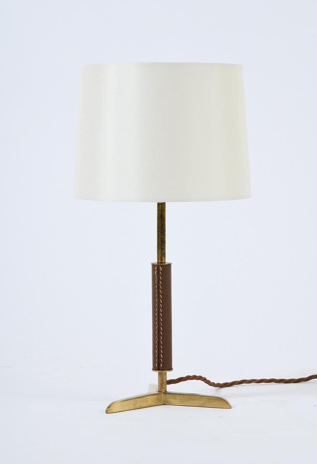 A brass and brown saddle stitched leather table lamp, in the manner of Jacques Adnet.
France, circa 1950.