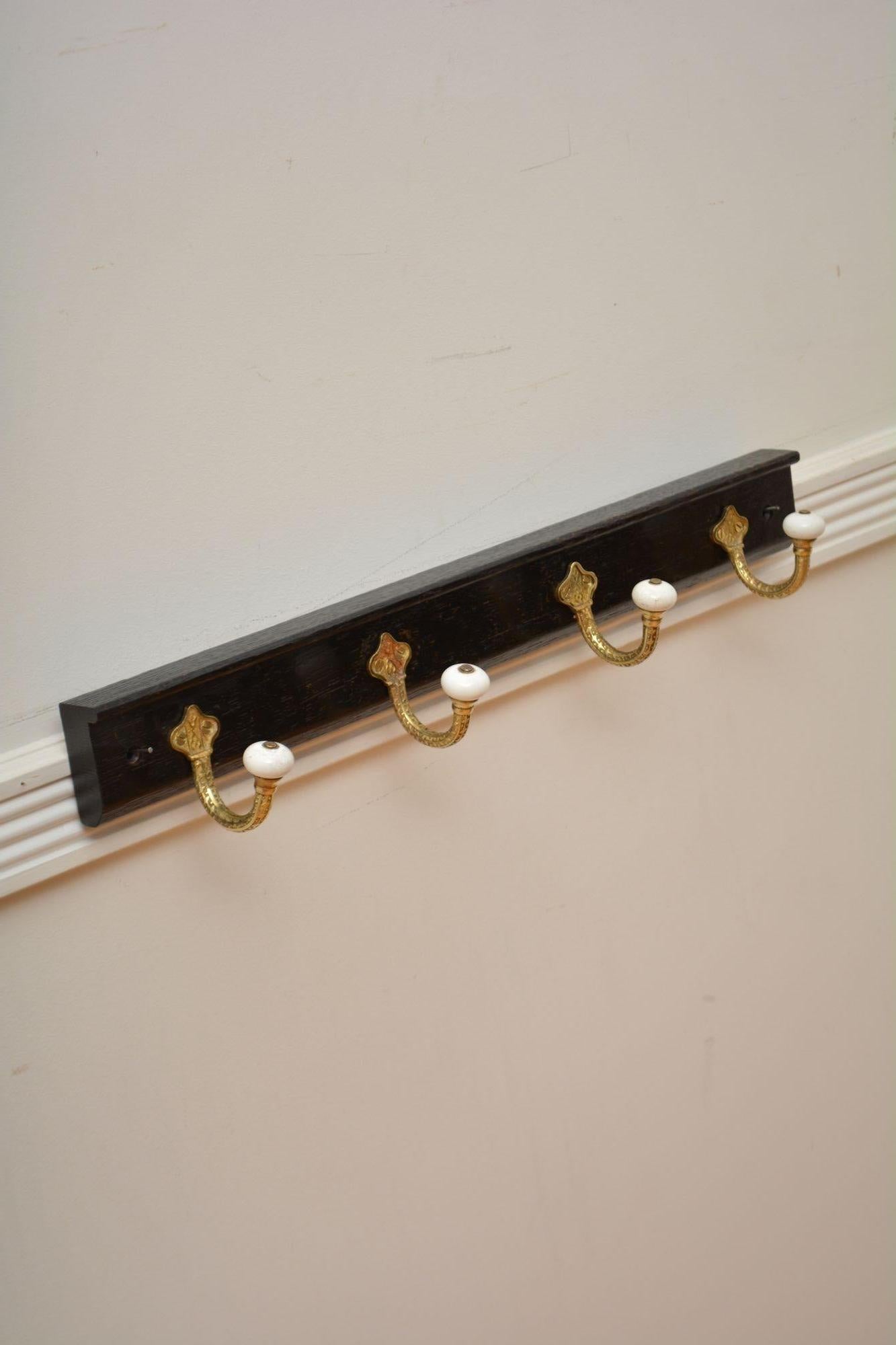 K0310 Elegant set of four Victorian brass and ceramic coat and hat hooks of very decorative design on ebonised solid oak backing with moulded top edge. Cleaned, polished and ready to place at home. 
H3.5