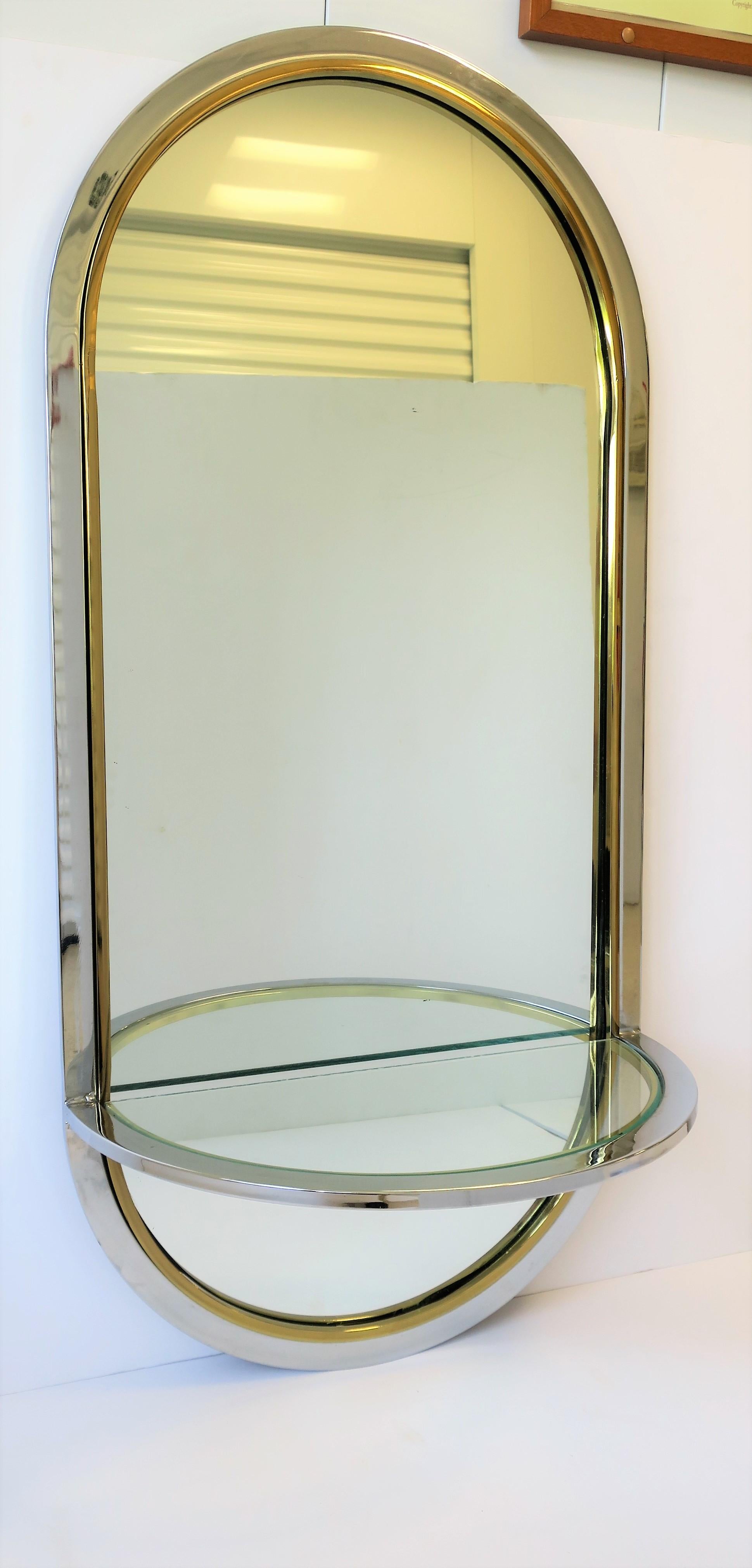A beautiful Postmodern or '70s Modern brass and chrome wall mirror, circa late-20th century. This wall mirror has a semi-circular top and bottom, and a demilune (half-moon) console shelf - demilune glass shelf is held by its chrome and brass frame