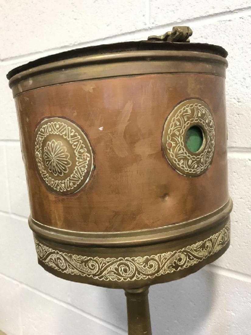 Brass and copper toned metal plant stand on scrolled tripod base, etched scroll design around lower part of top and circular etched design on body. Removable interior metal pot with side holes and brass toned metal accents on hinges. Some dents to