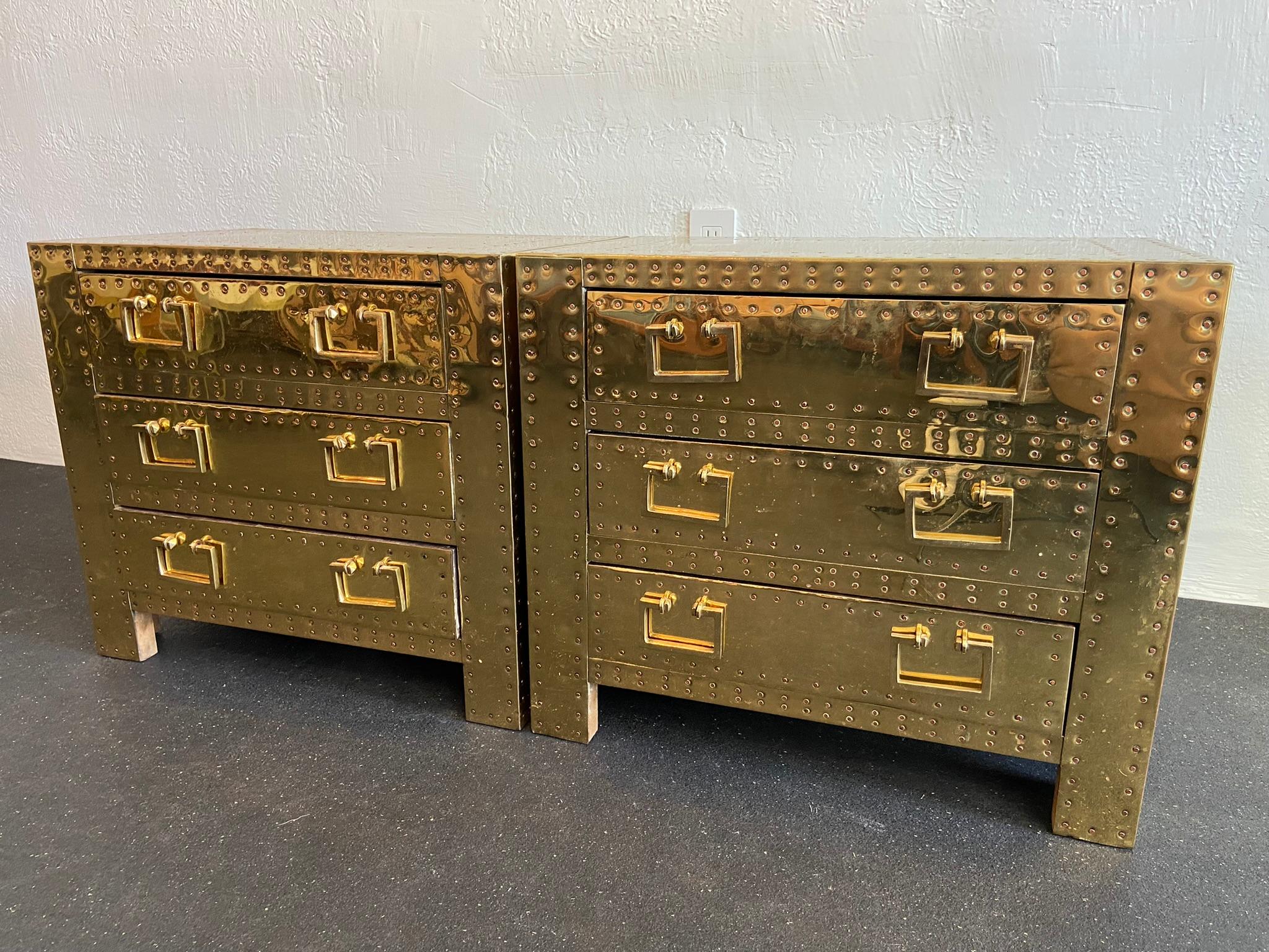 Pair of brass and copper clad chest by Sarreid LTD. Polished within the last few years. Brass applied over wood frames with copper brads. Heavy, solid construction. Dents and marks are present, consistent with normal wear from use on these pieces.