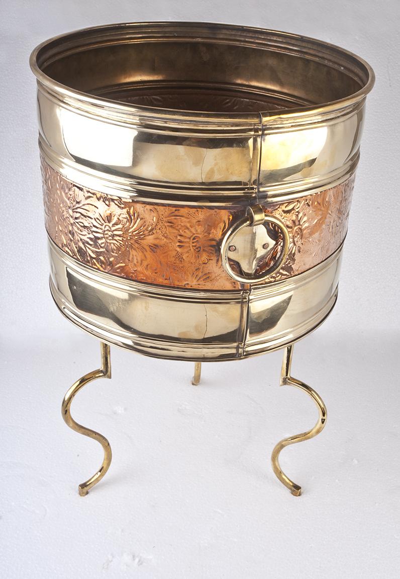A brass planter with embossed copper relief through the center on a custom made brass stand. Two brass rings on opposing sides. English, 1970s. Measures: Overall height 19