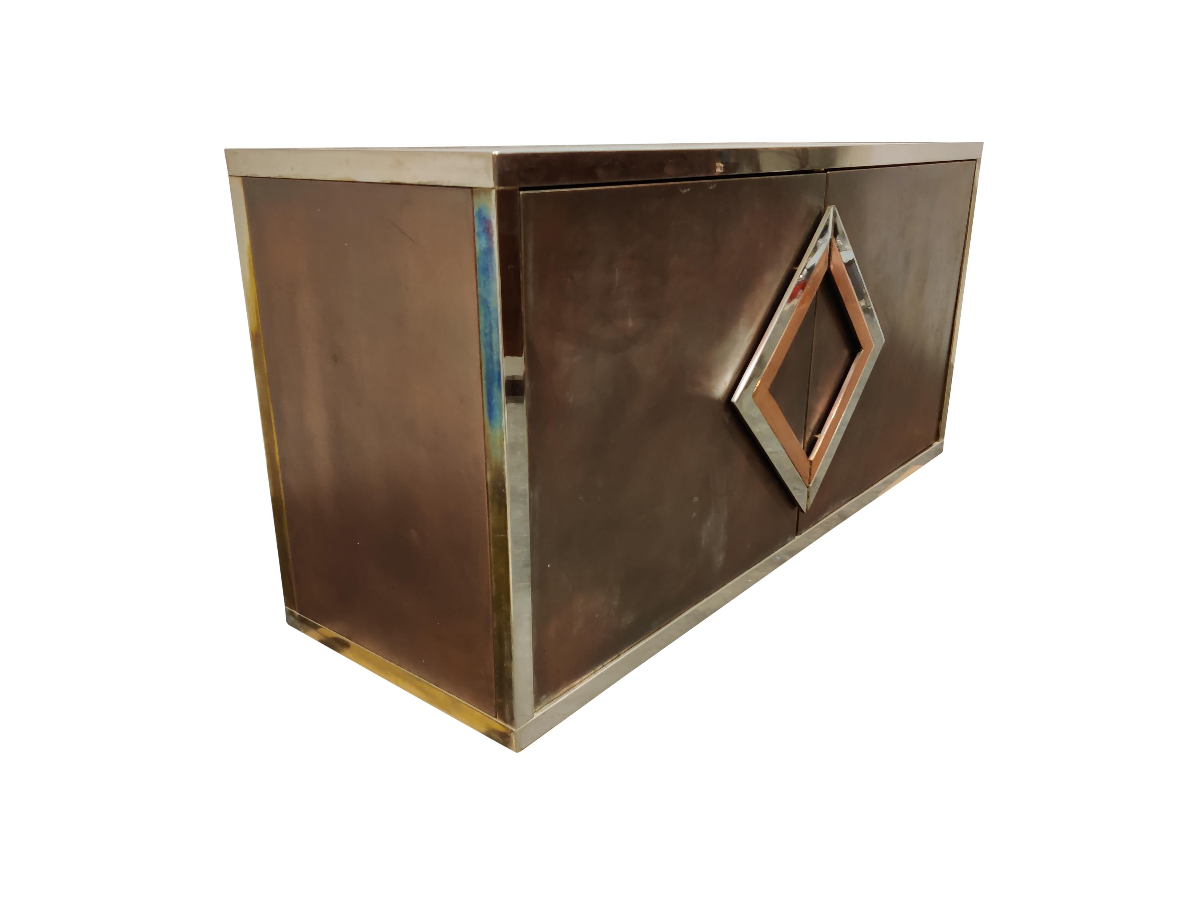 Vintage red copper, brass and chrome sideboard by Maison Jansen.

The cabinet has two large doors with unique geometrical handles and glass shelves inside.

Its made from a brass, chrome frame and red copper panels. 

Although the brass is